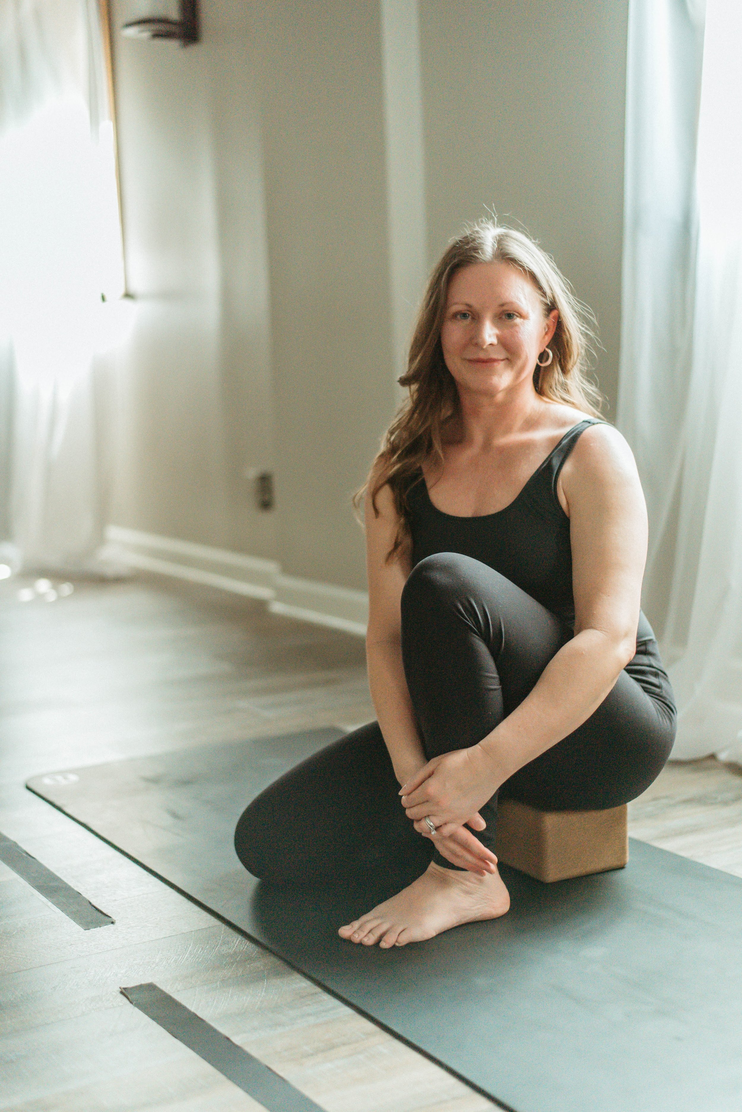 A woman sitting cross-legged on the floor with one hand on her chest and the other on her stomach, looking upward with a thoughtful expression.