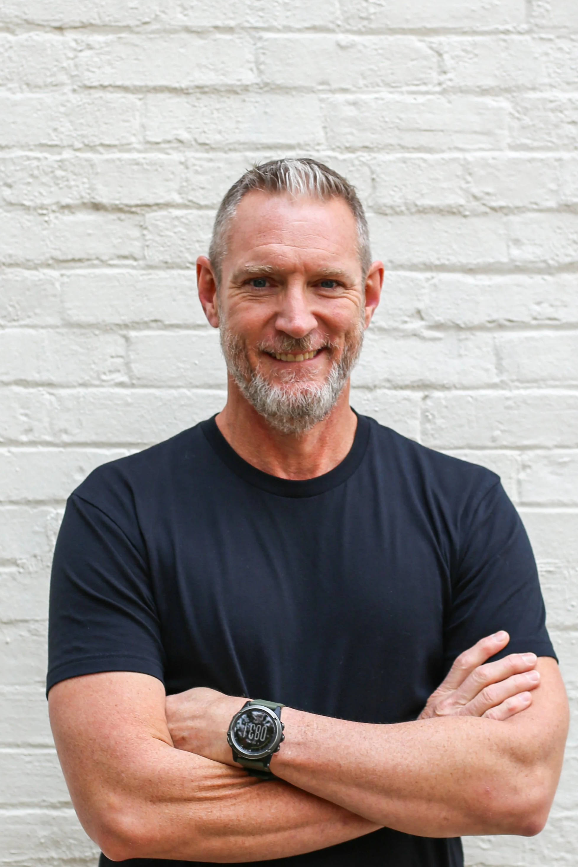 William Walker, life coach, smiling with arms crossed in front of a white brick wall.