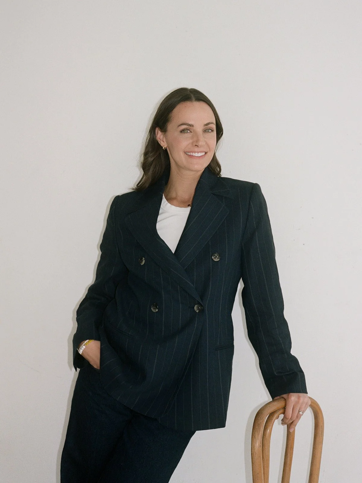 Woman leans against a bentwood chair in a pinstripe suit for a branding portrait