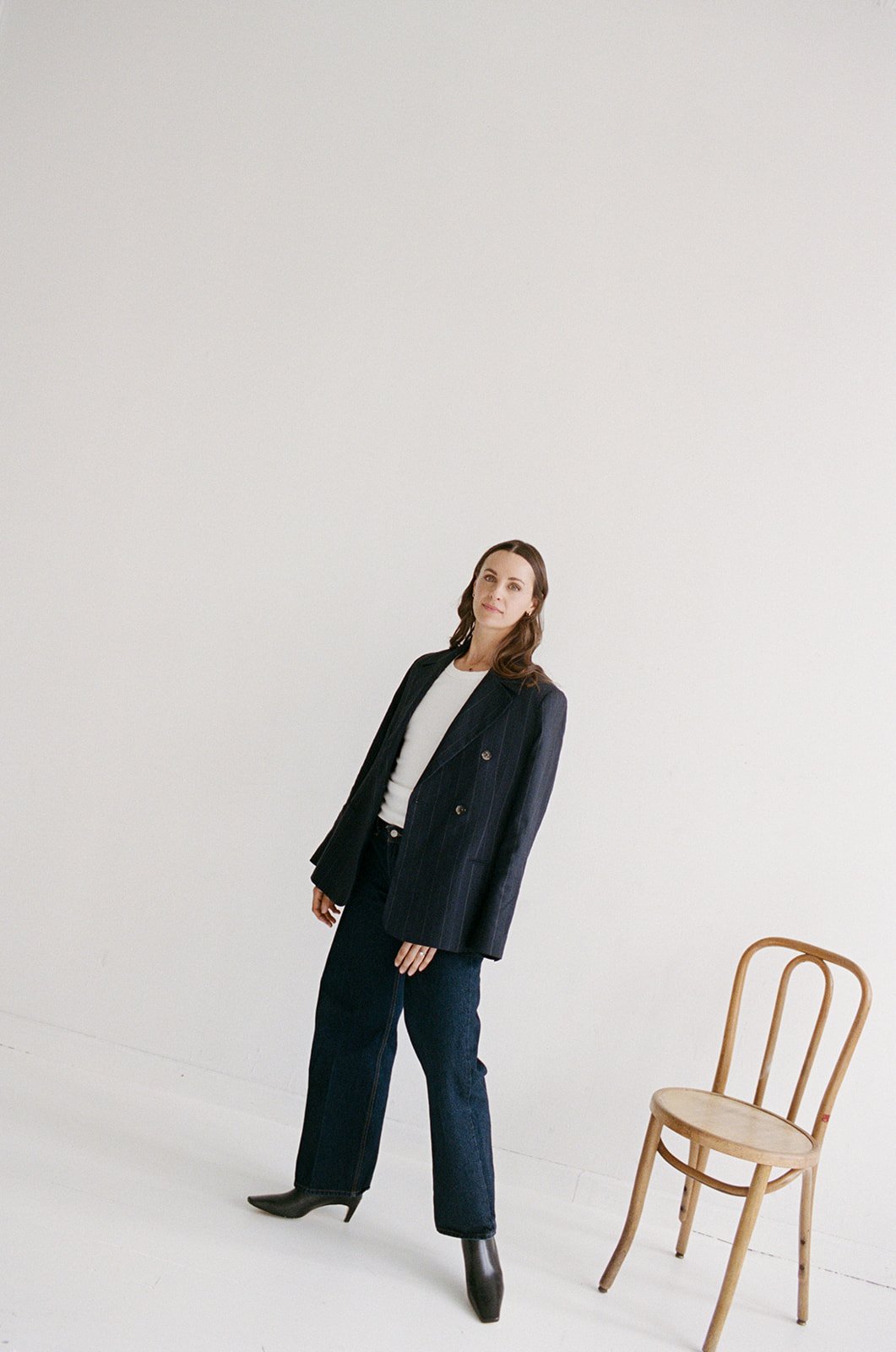 Full length film portrait of a woman in a tailored blazer standing in a white studio