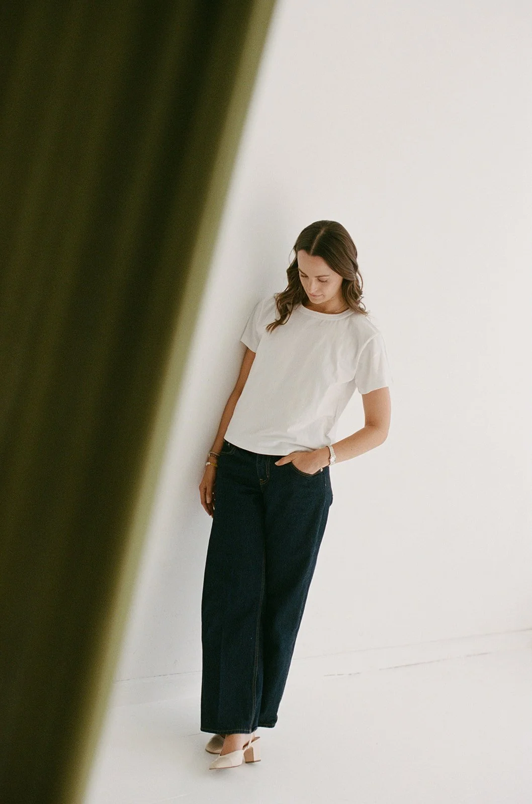 Candid film portrait of a woman in a white t-shirt framed through a gap in a dark curtain