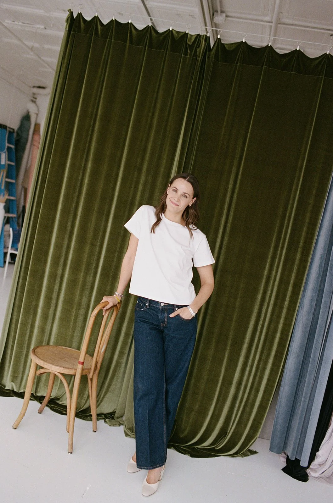 Full length film portrait in a white t-shirt and denim against an olive green velvet curtain