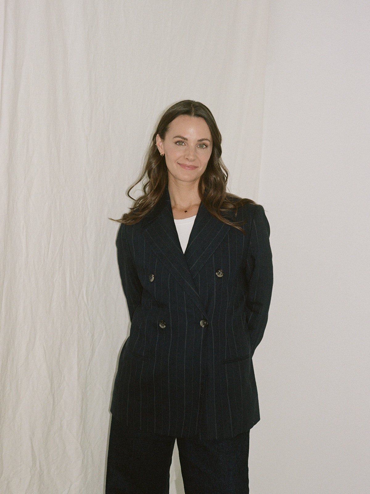 Woman in a pinstripe double-breasted blazer poses against a neutral curtain backdrop for a Chicago film branding session