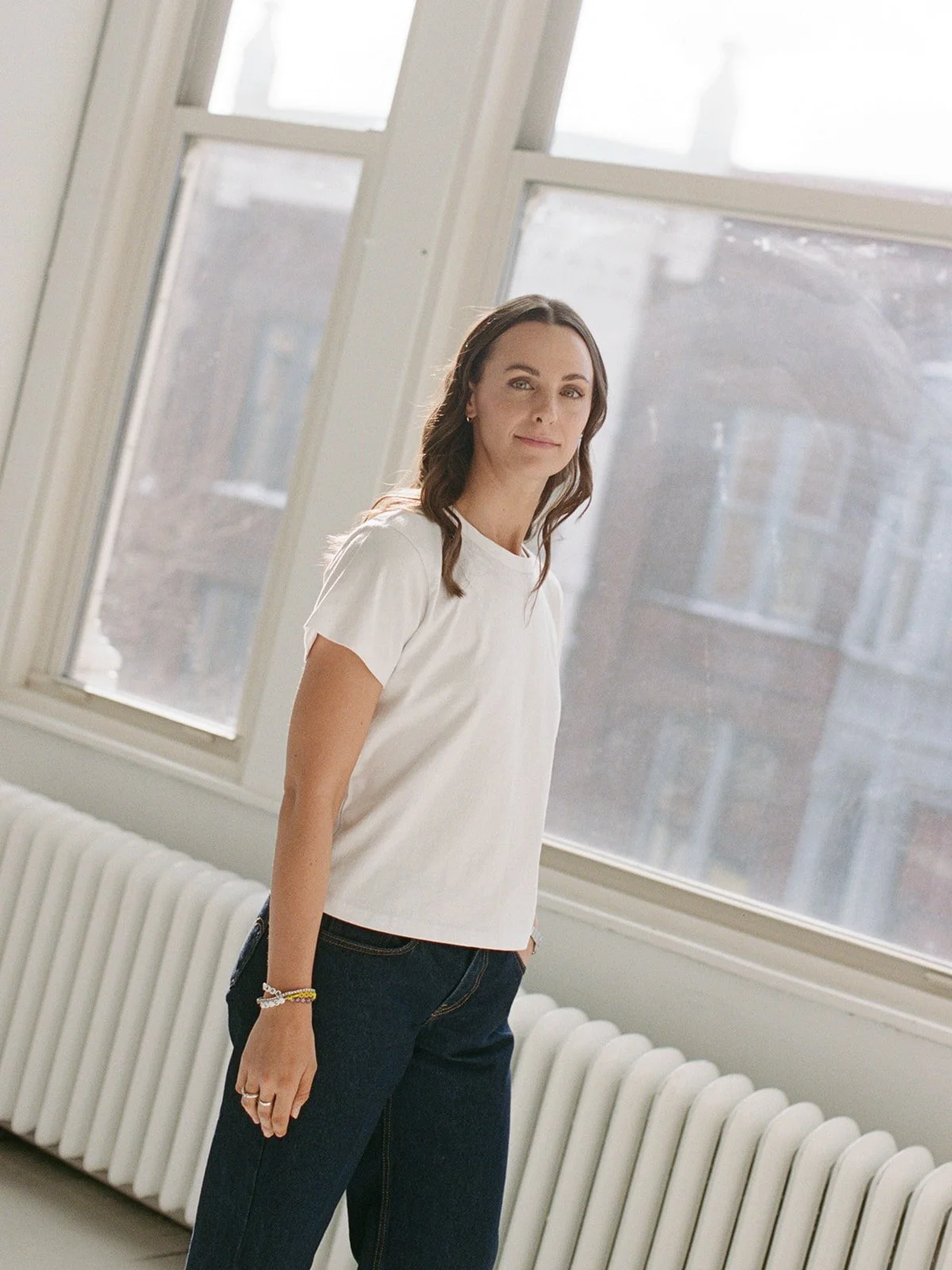Woman in a white t-shirt poses by a sunlit window with the Chicago skyline visible outside