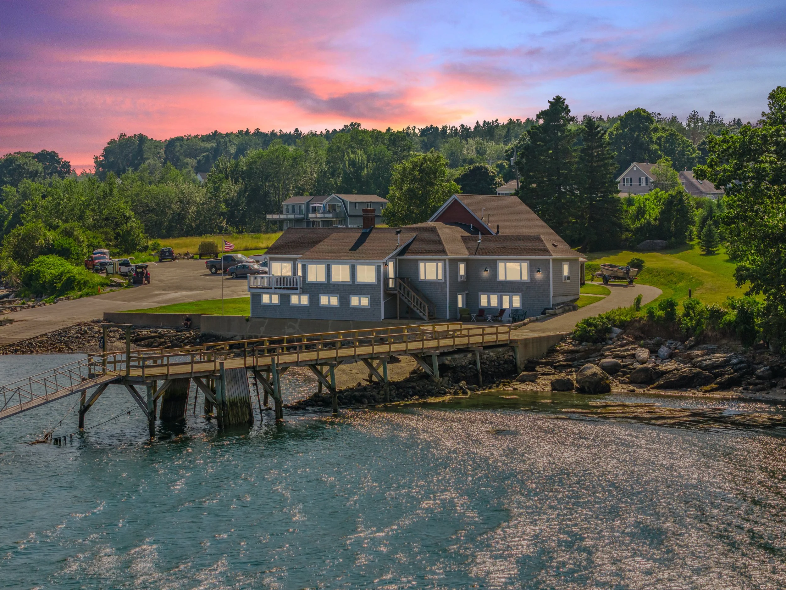 A house by the water with a small bridge, parked boats, and a sunset sky.
