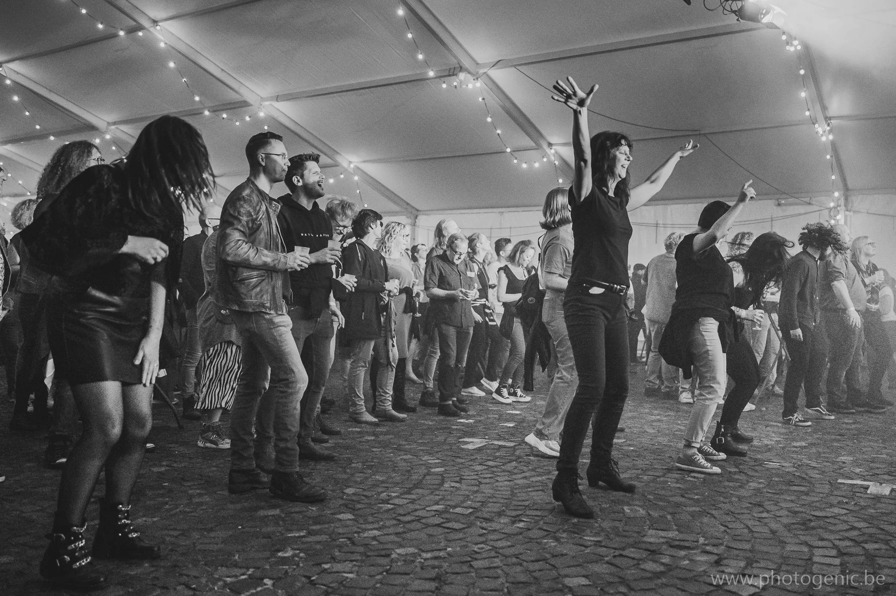 Mensen dansen op een feestje of concert onder een tent met feestverlichting, zwart-wit foto.