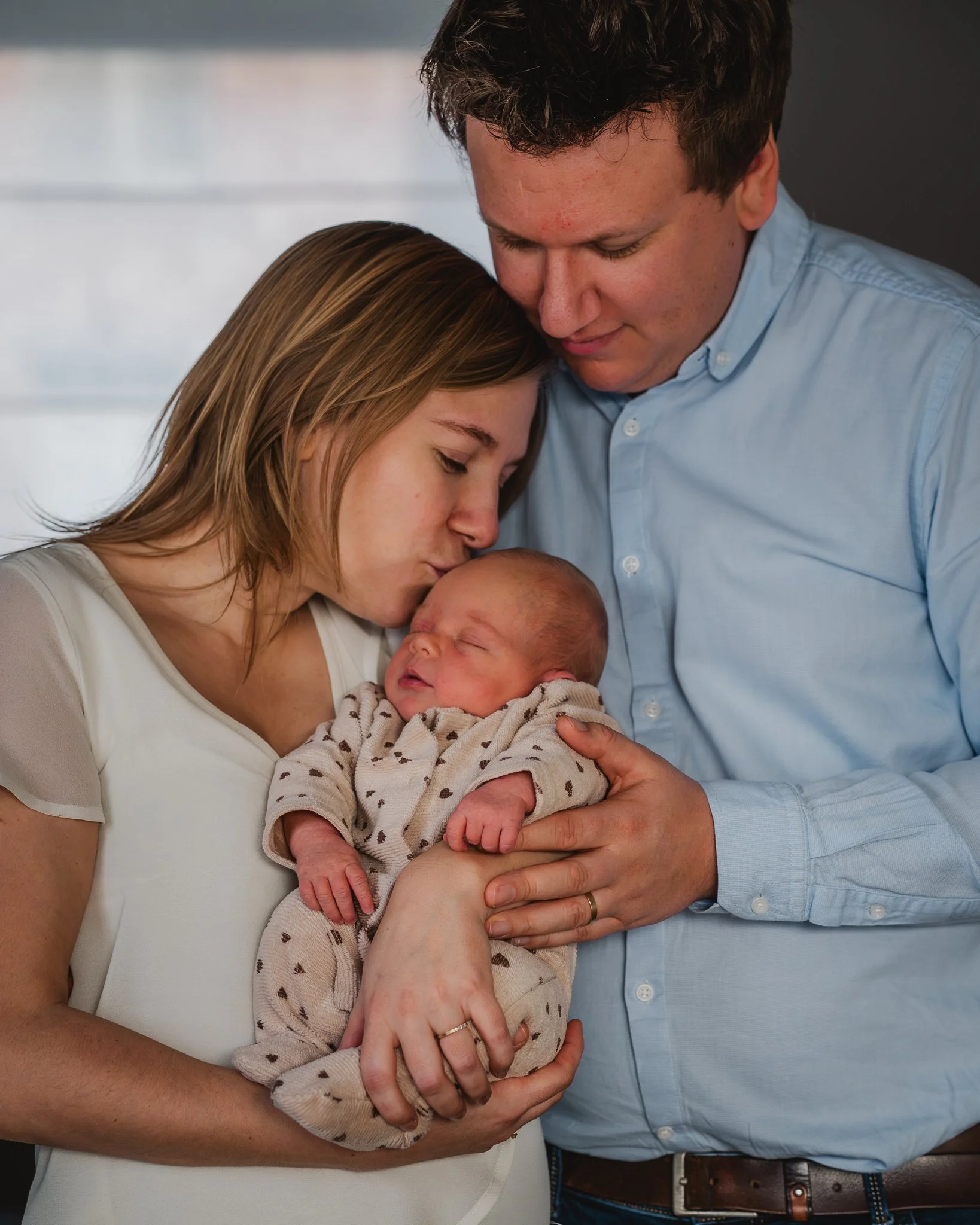 Baby die gekoesterd wordt door ouders, vrouw kuste baby en man houdt baby in zijn armen in een lichte kamer.