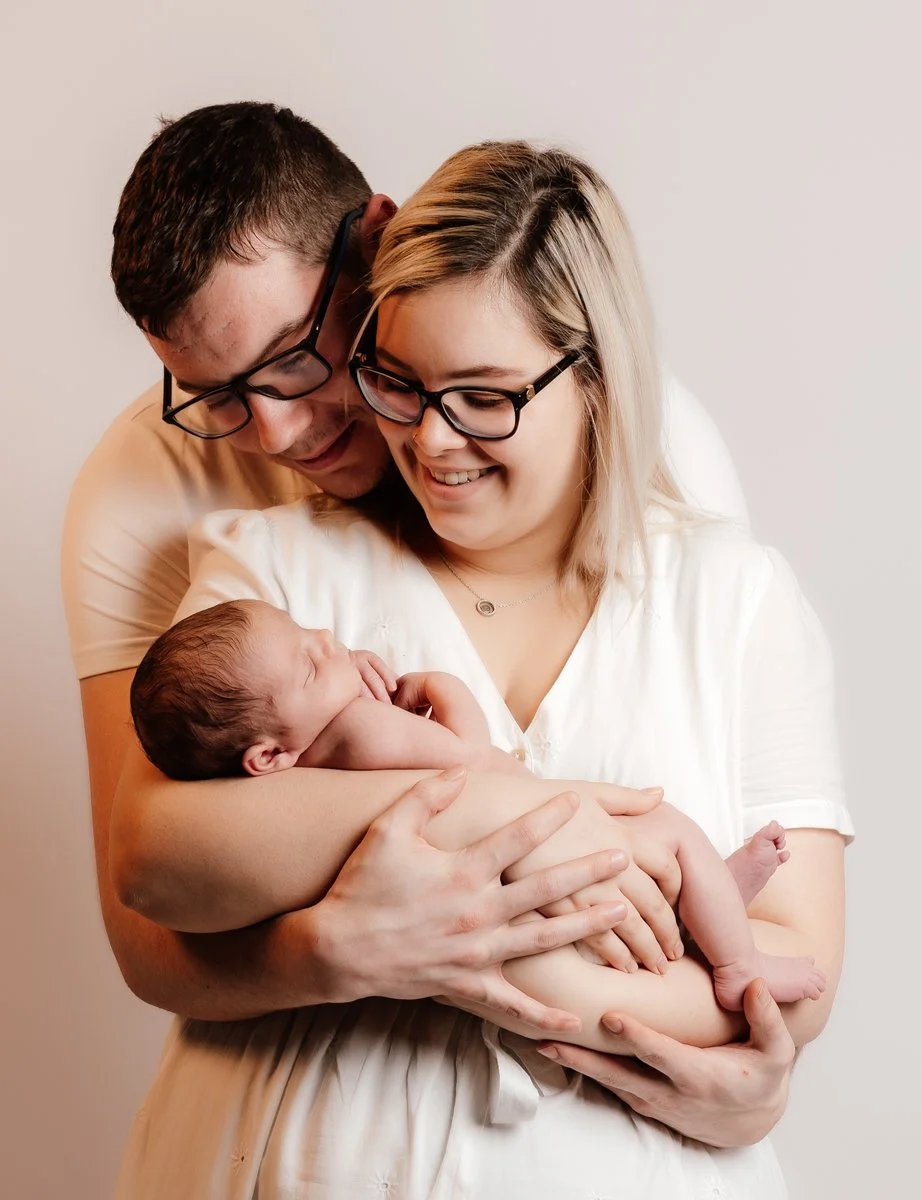 Een gezin met een baby, de ouders kijken liefdevol naar de baby terwijl ze hem vasthouden.