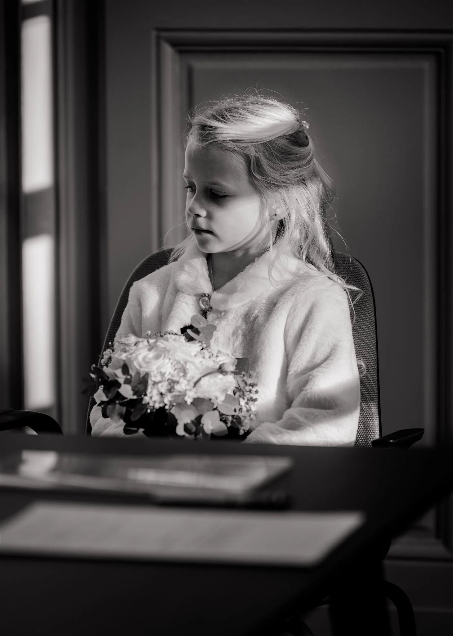 Zweedse jonge meisje zit op een stoel, houdt een boeket bloemen vast en kijkt terzijde, in zwart-wit.