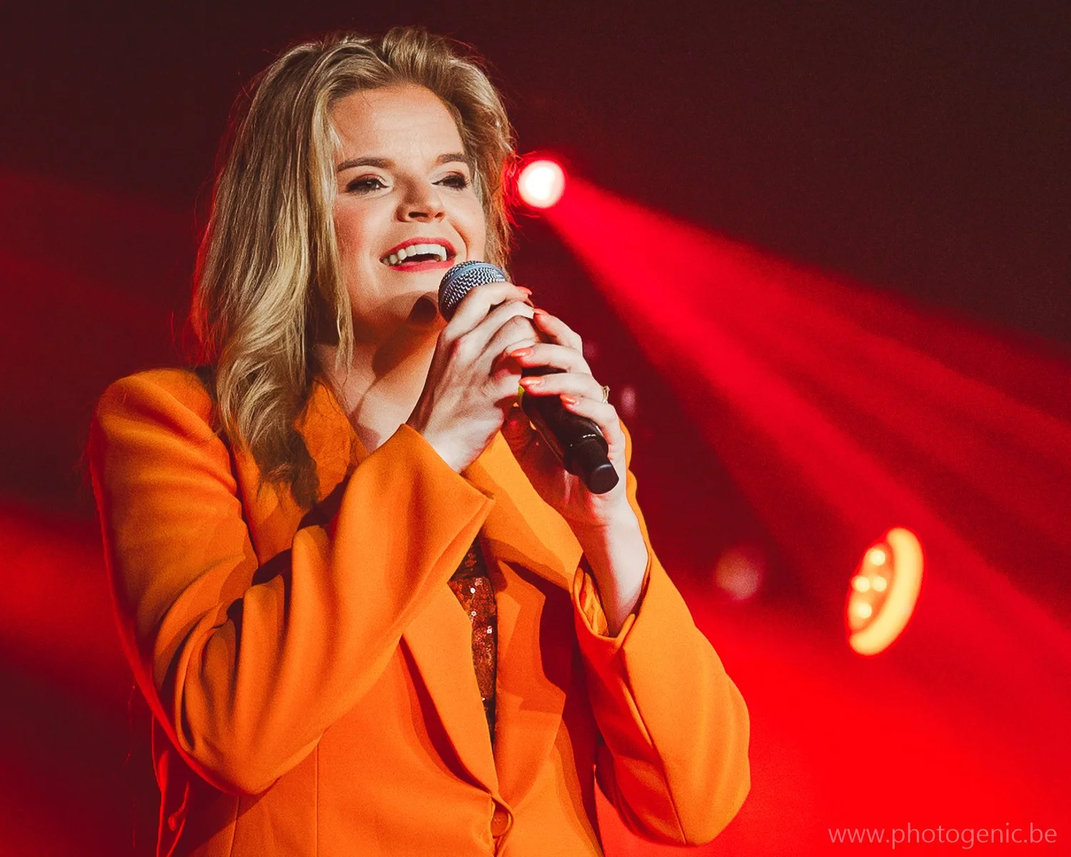 Vrouw zingt met microfoon op een podium met rode verlichting.