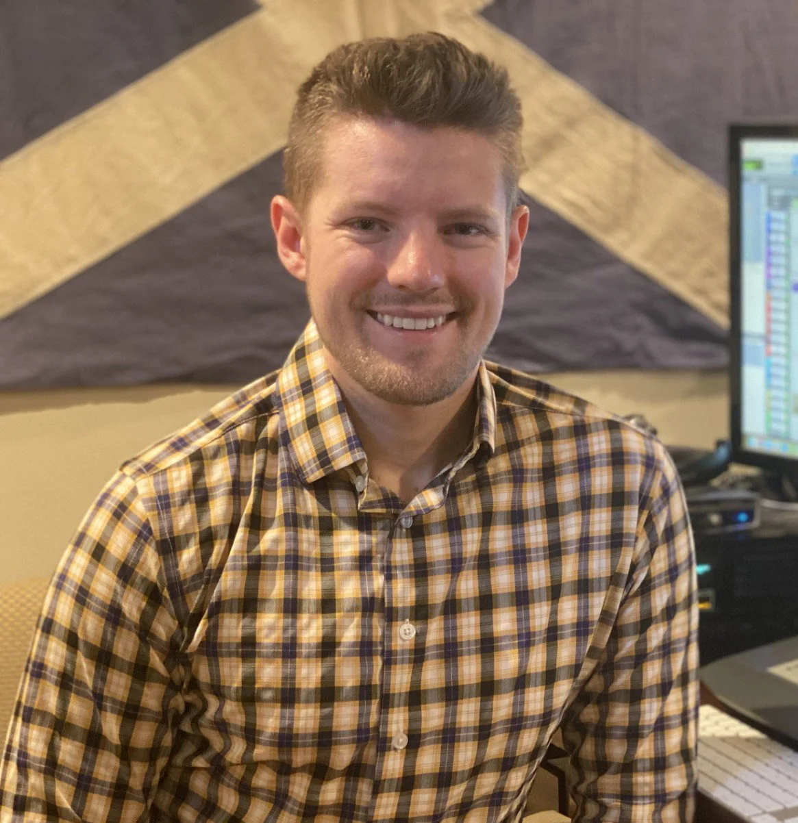Steve sitting at his desk. He is smiling at the camera. A Scottish flag is on the wall behind him