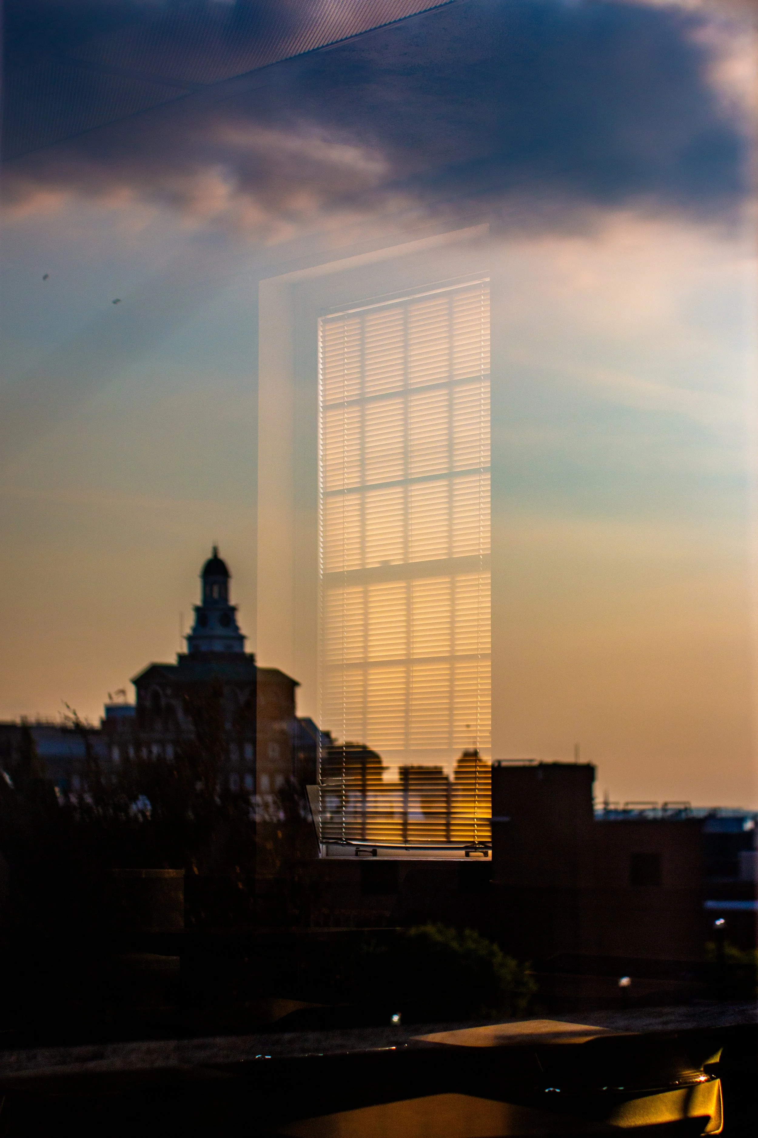 Through one classroom window, another is framed, reflecting a building and the golden hour sky on July 12, 2025, in Syracuse, N.Y.