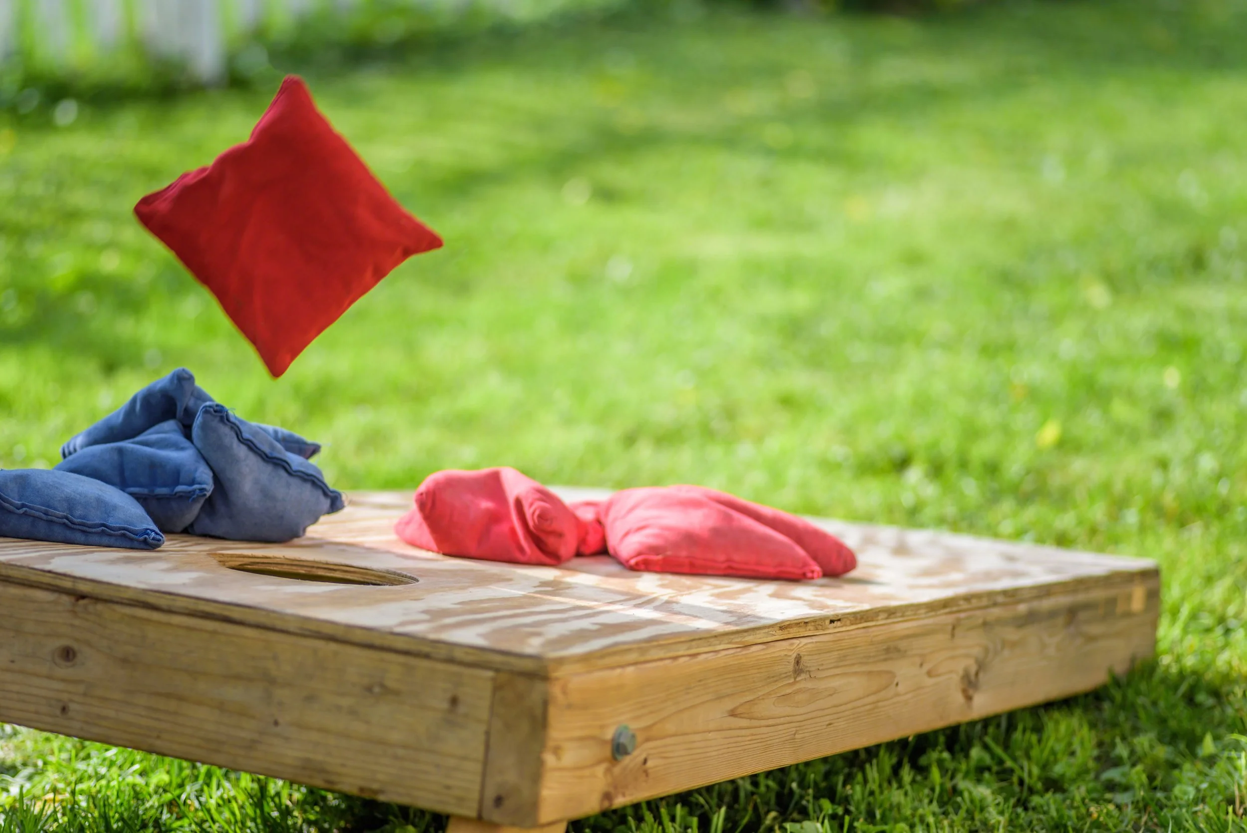 Colorful bean bags and pillows on a wooden board outdoors with green grass in the background