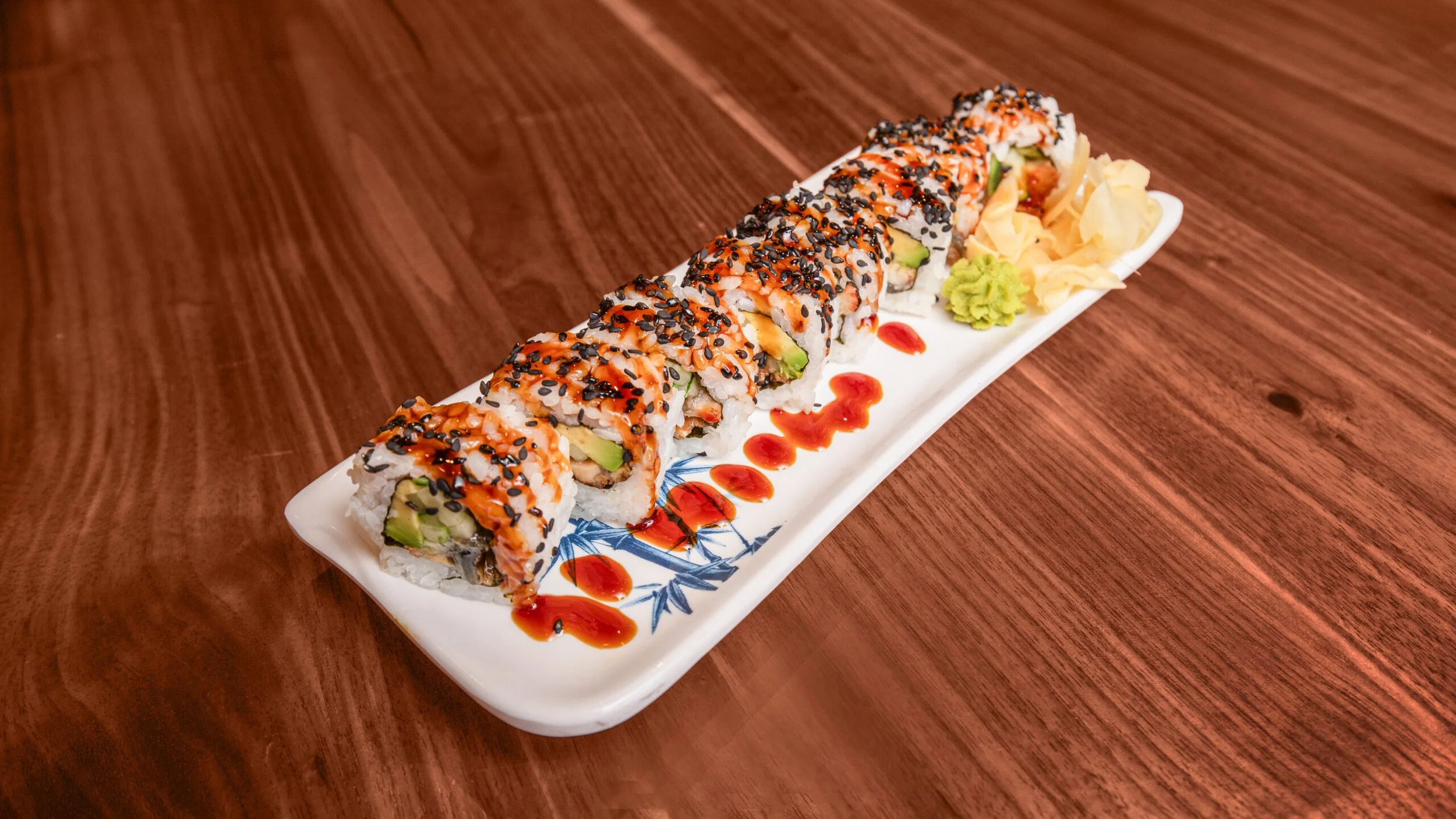 Sushi roll on a long rectangular plate with soy sauce, wasabi, and pickled ginger, placed on a wooden table.