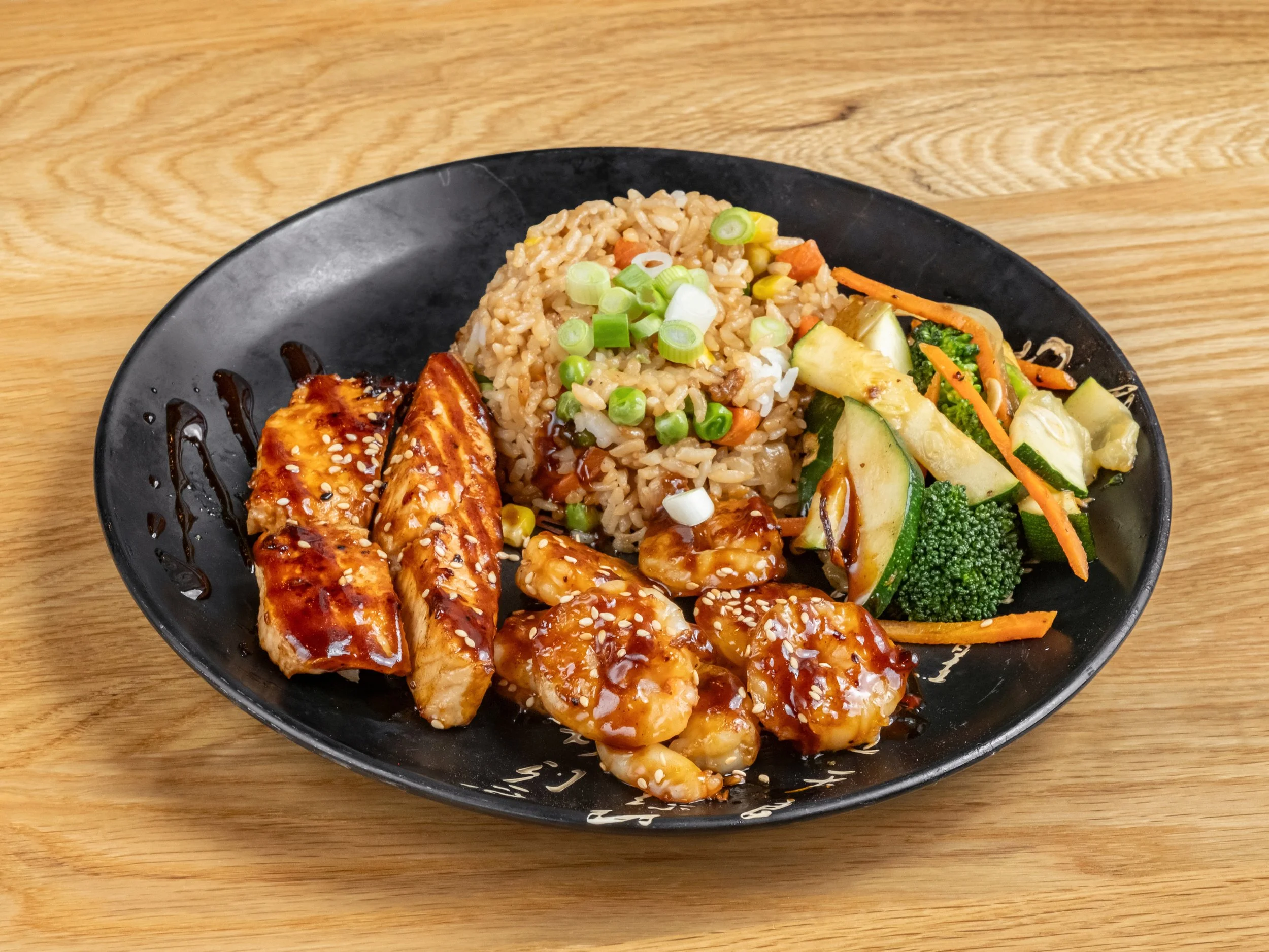 Black bowl with chicken, shrimp, fried rice, and mixed vegetables, on a wooden table.