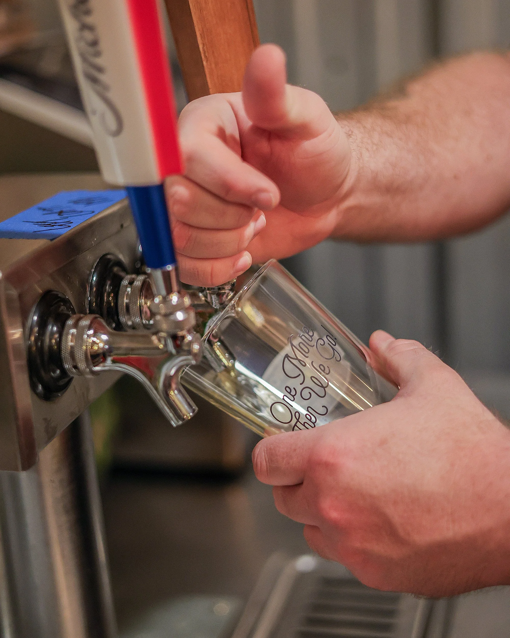 Close-up of a person's hand holding a glass bottle with writing on it, filling a vending machine with a liquid, possibly hand sanitizer or sanitizer fluid.