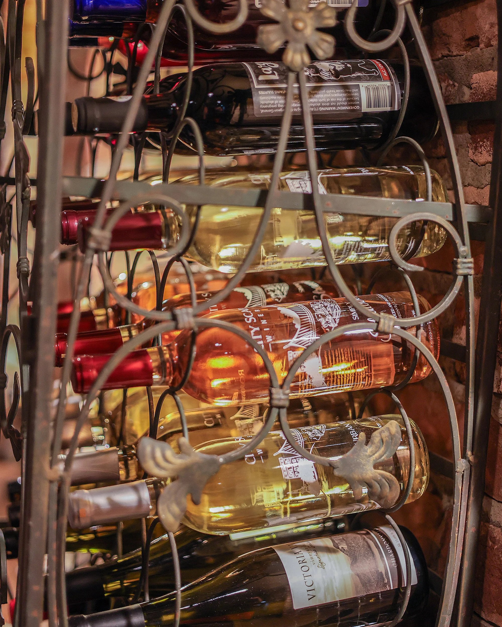 Shelf with multiple bottles of white wine with labels, enclosed in a wire rack, against a brick wall background.