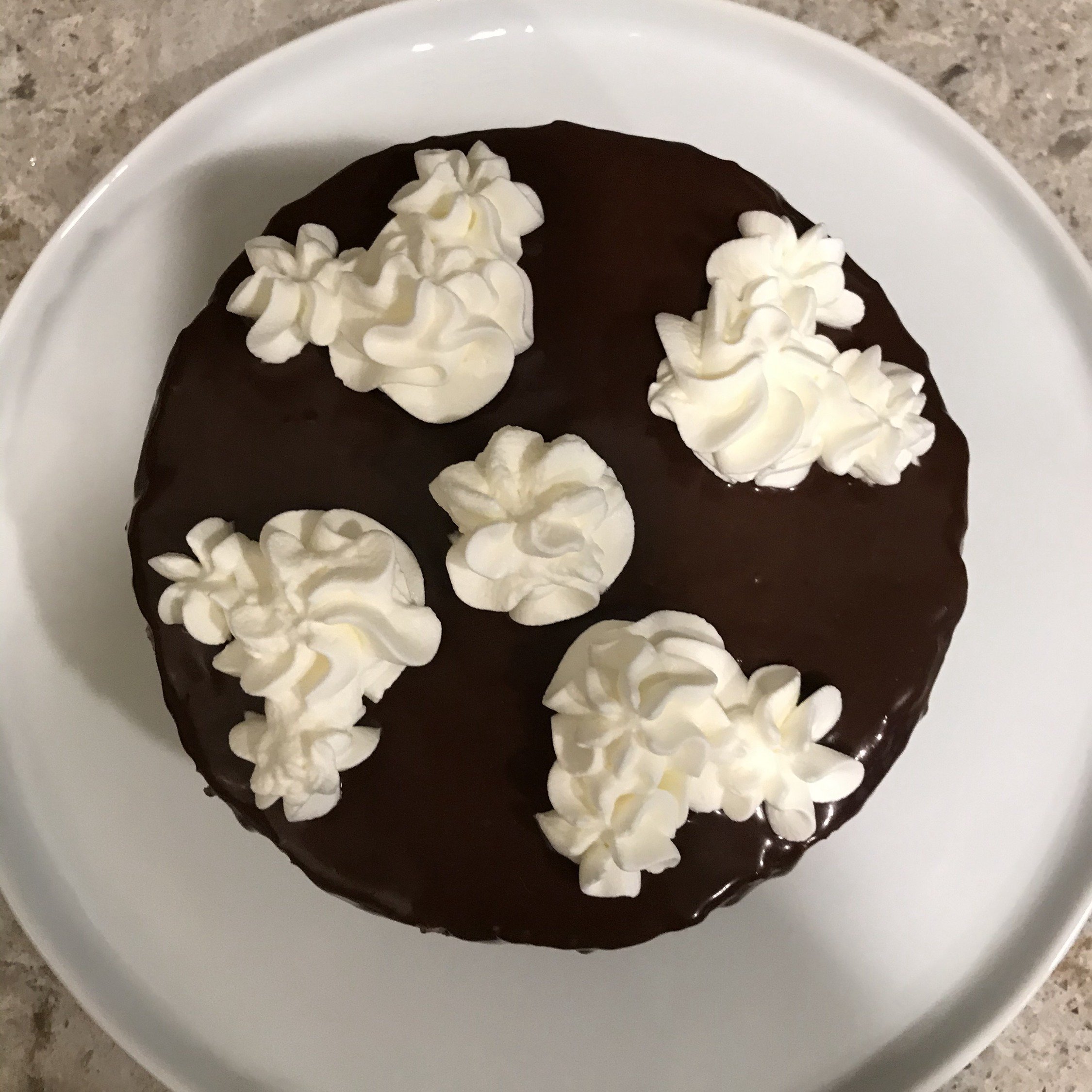  Top view of fully iced and ganached cake. Four mickey shaped dollops of whipped cream on top with a dollop of whipped cream in the center 