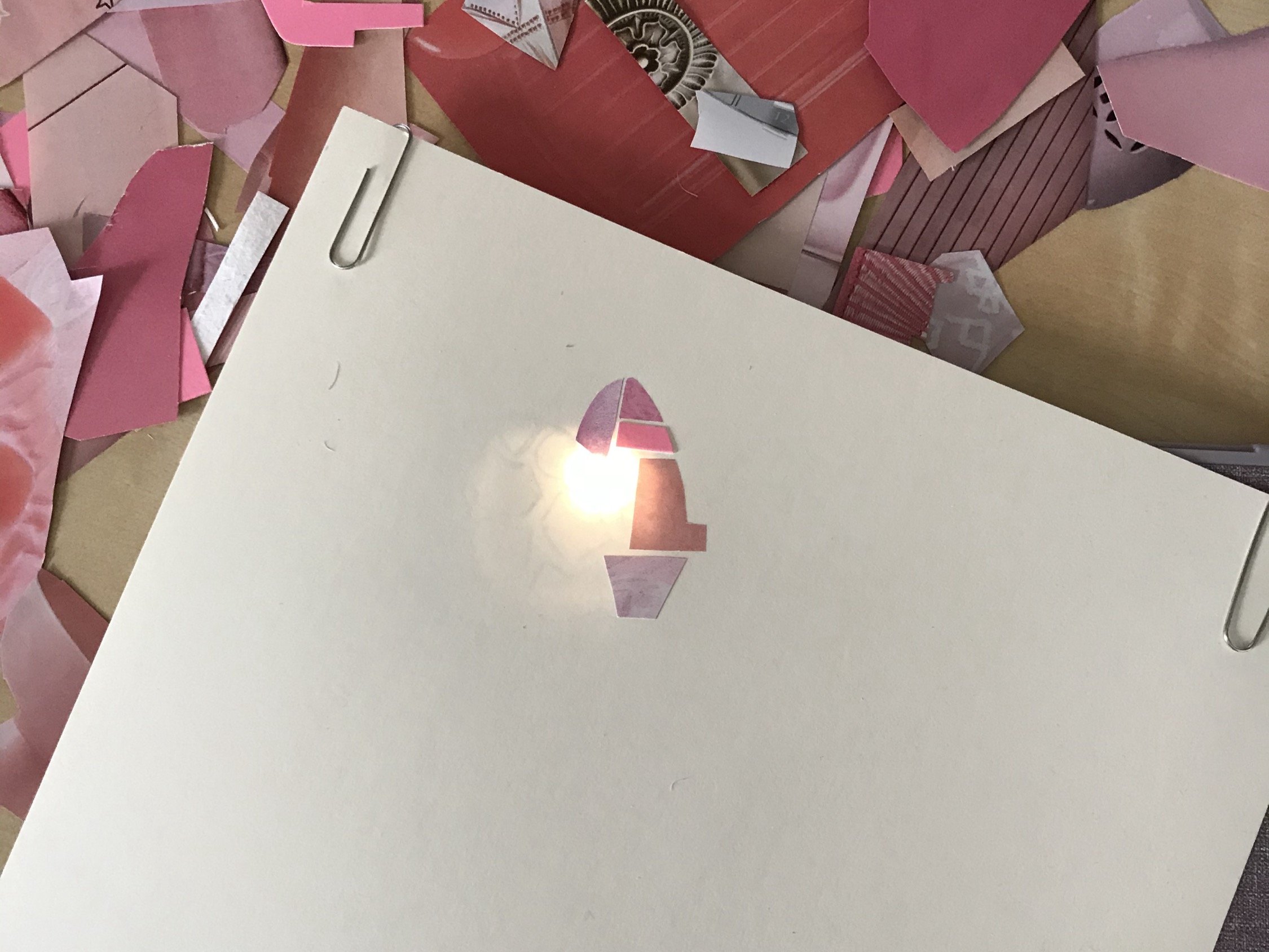  Paper with a paper clip in the corner with some pink scraps of paper glued on on top of a flashlight 