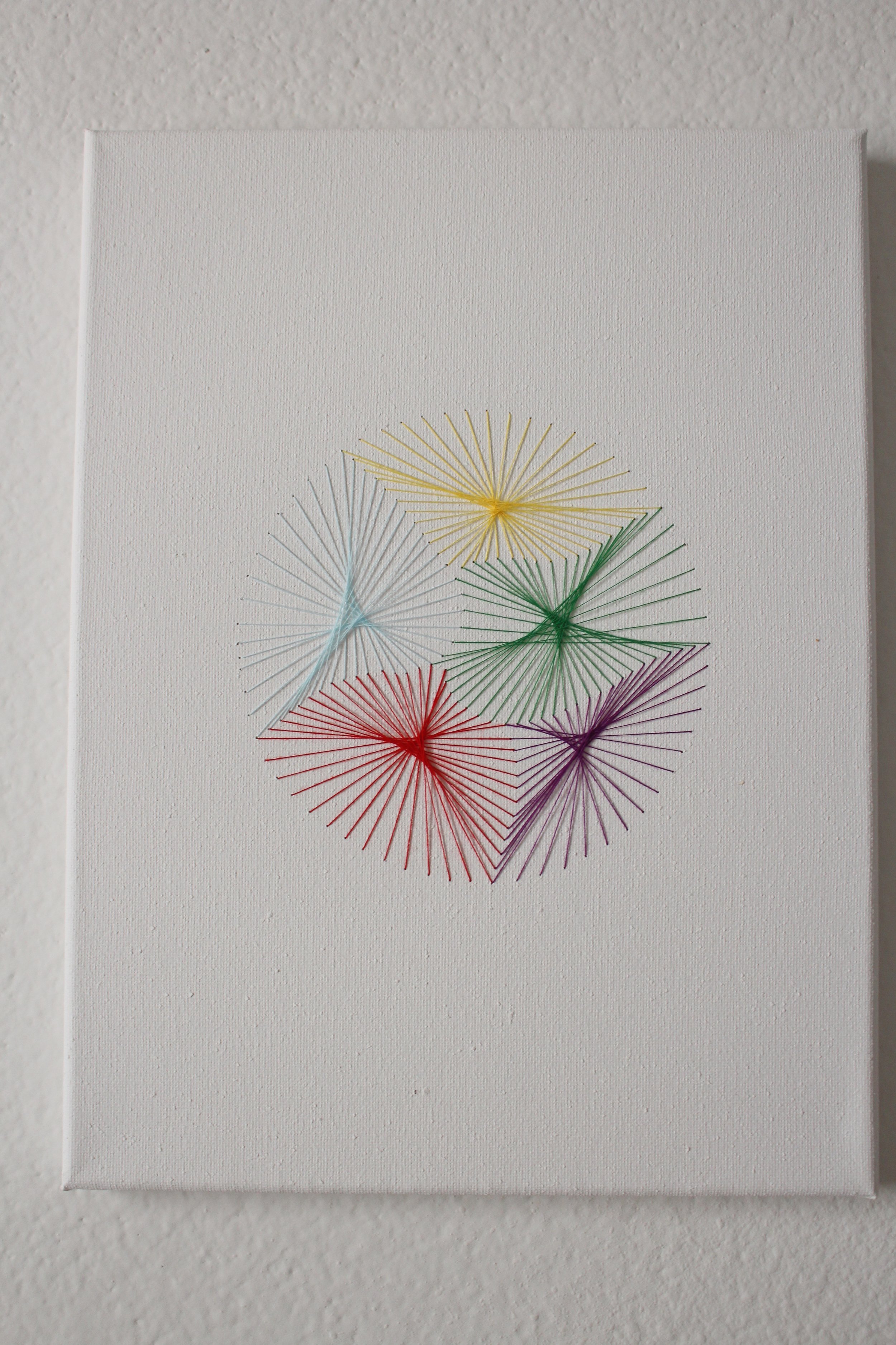  Red, blue, green, yellow, and purple threads sewn into a canvas in the shape of a ball 