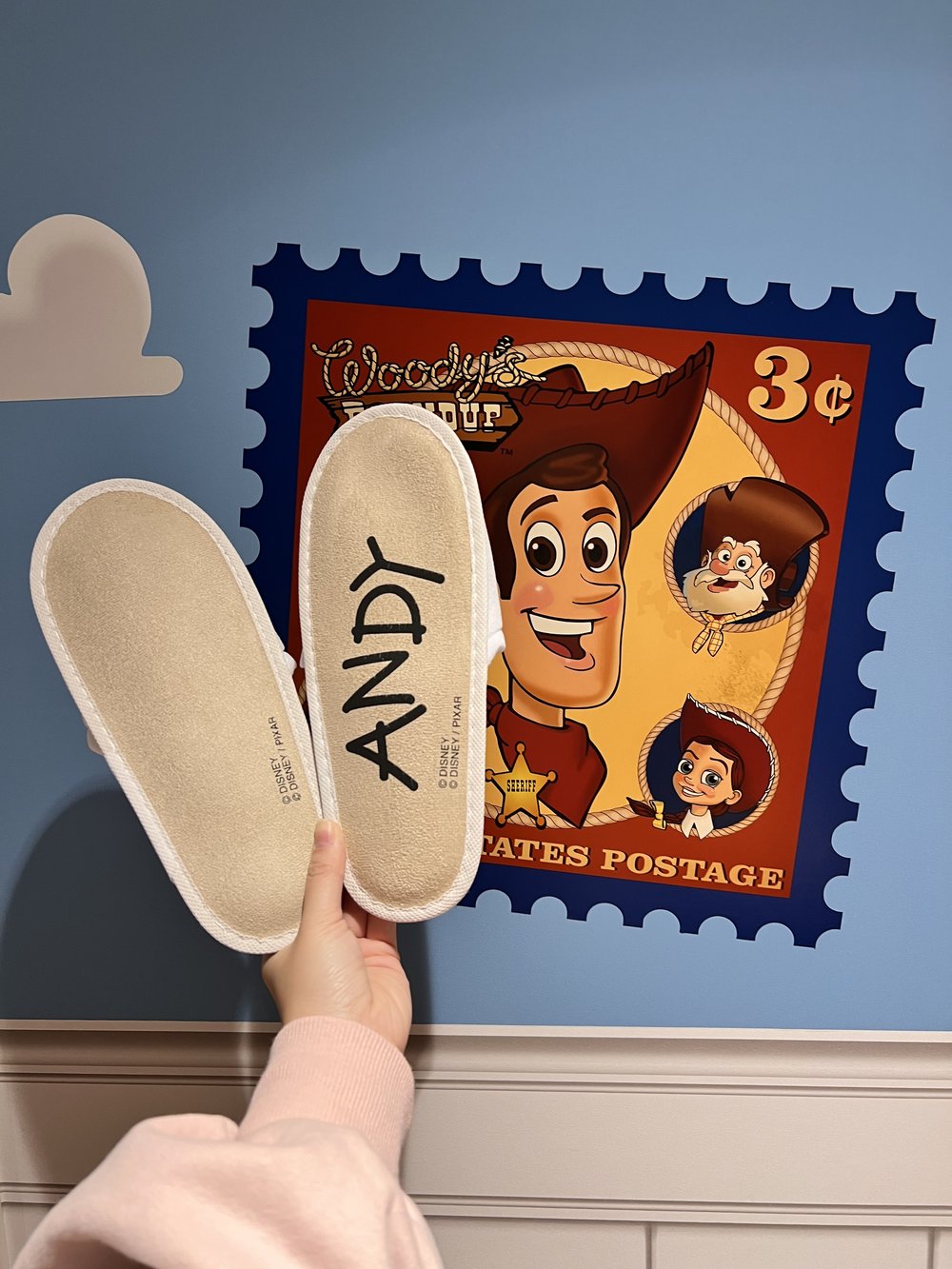  The bottom of the house slippers with the word ANDY written on the bottom in front of a Woody poster 