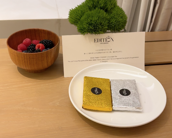  Table with a small bowl of fruits and a plate of chocolates with a welcome sign 