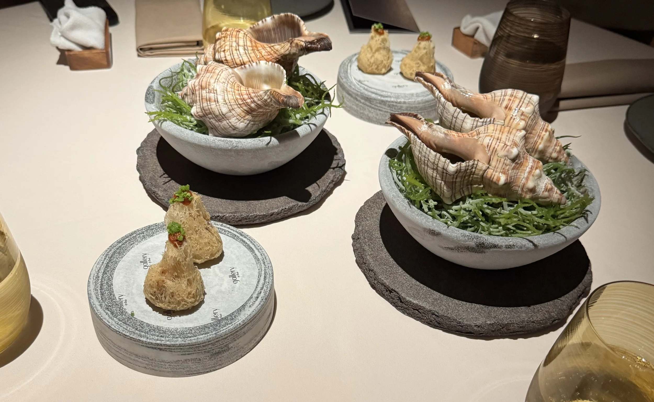 4 large conch shells on a bed of greens next to two plates of fried lobster puffs