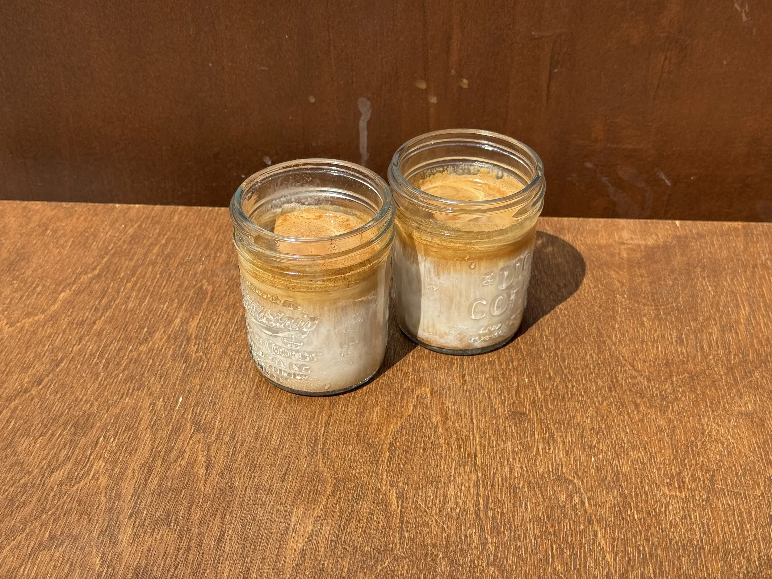 Two clear mason jars on a wooden bench with white milk layered with coffee on top