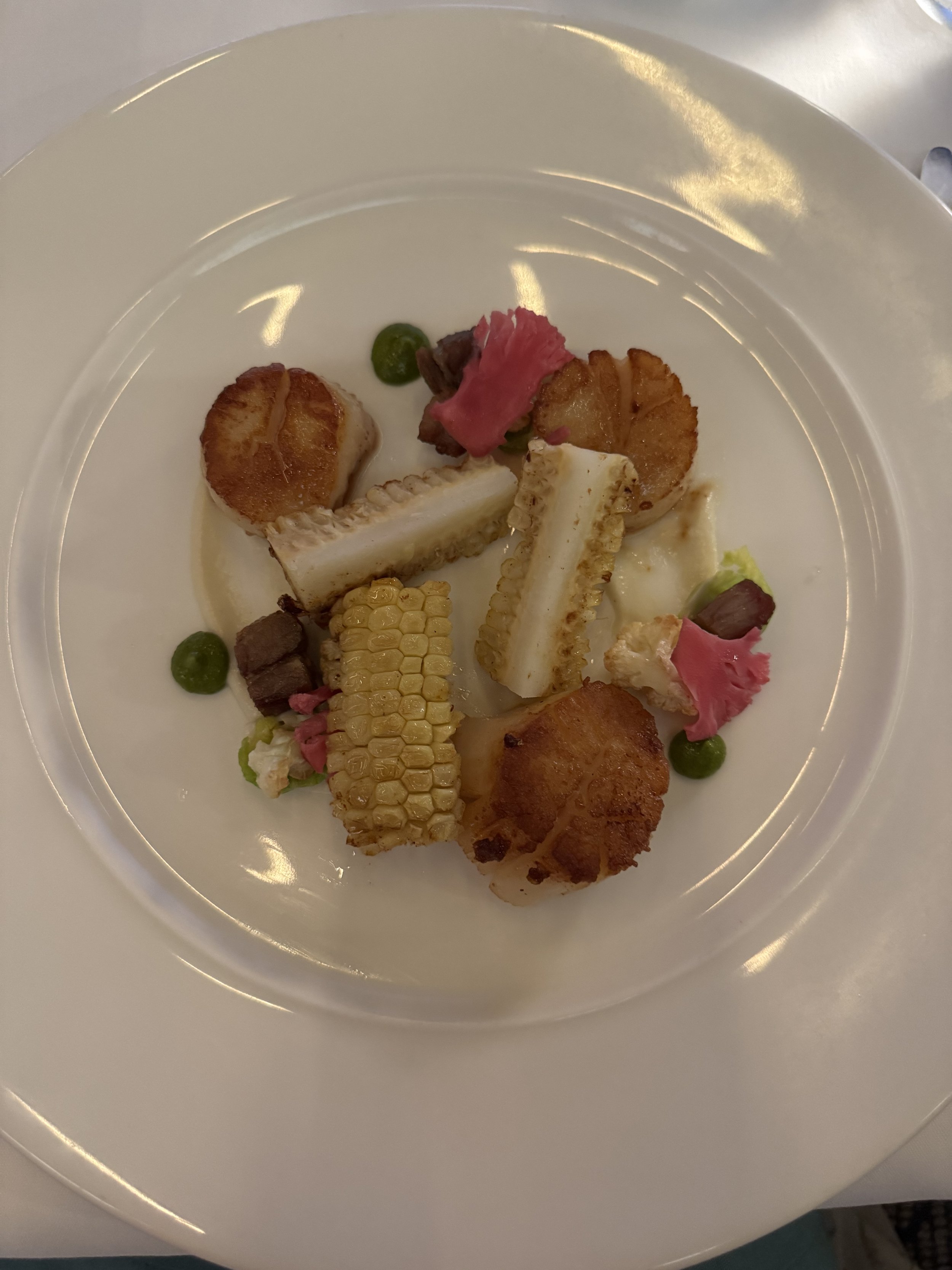 three seared scallops with pork, corn on the cob sliced in three and cauliflower