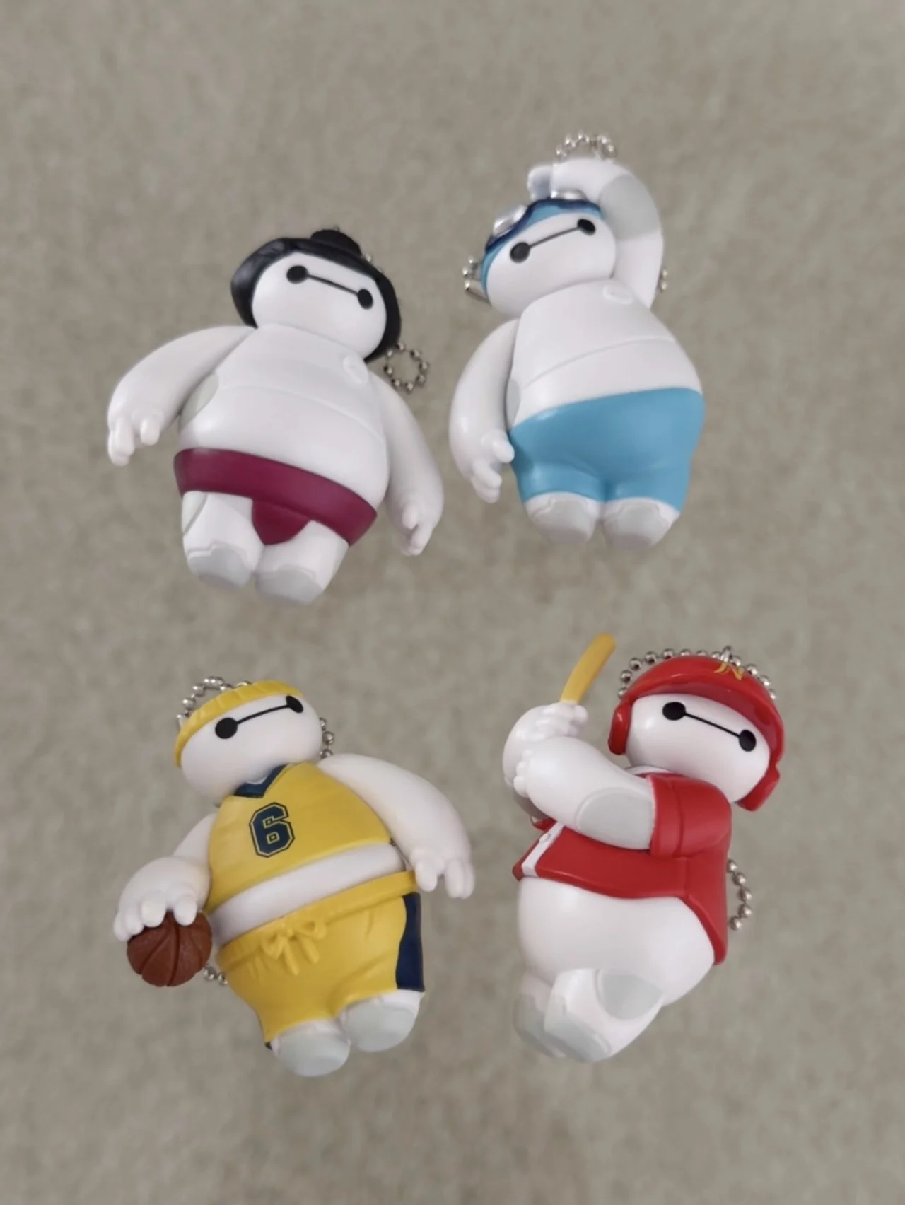 4 variations of Baymax keychains wearing a sumo outfit, swimming, basketball, and baseball