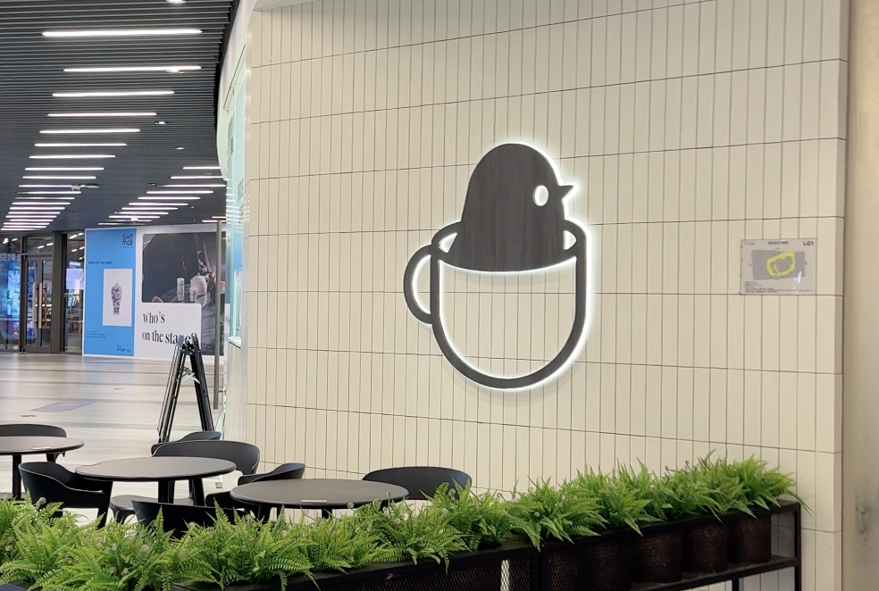 black colored bird sitting in a cup logo on a white wall behind black tables and chairs
