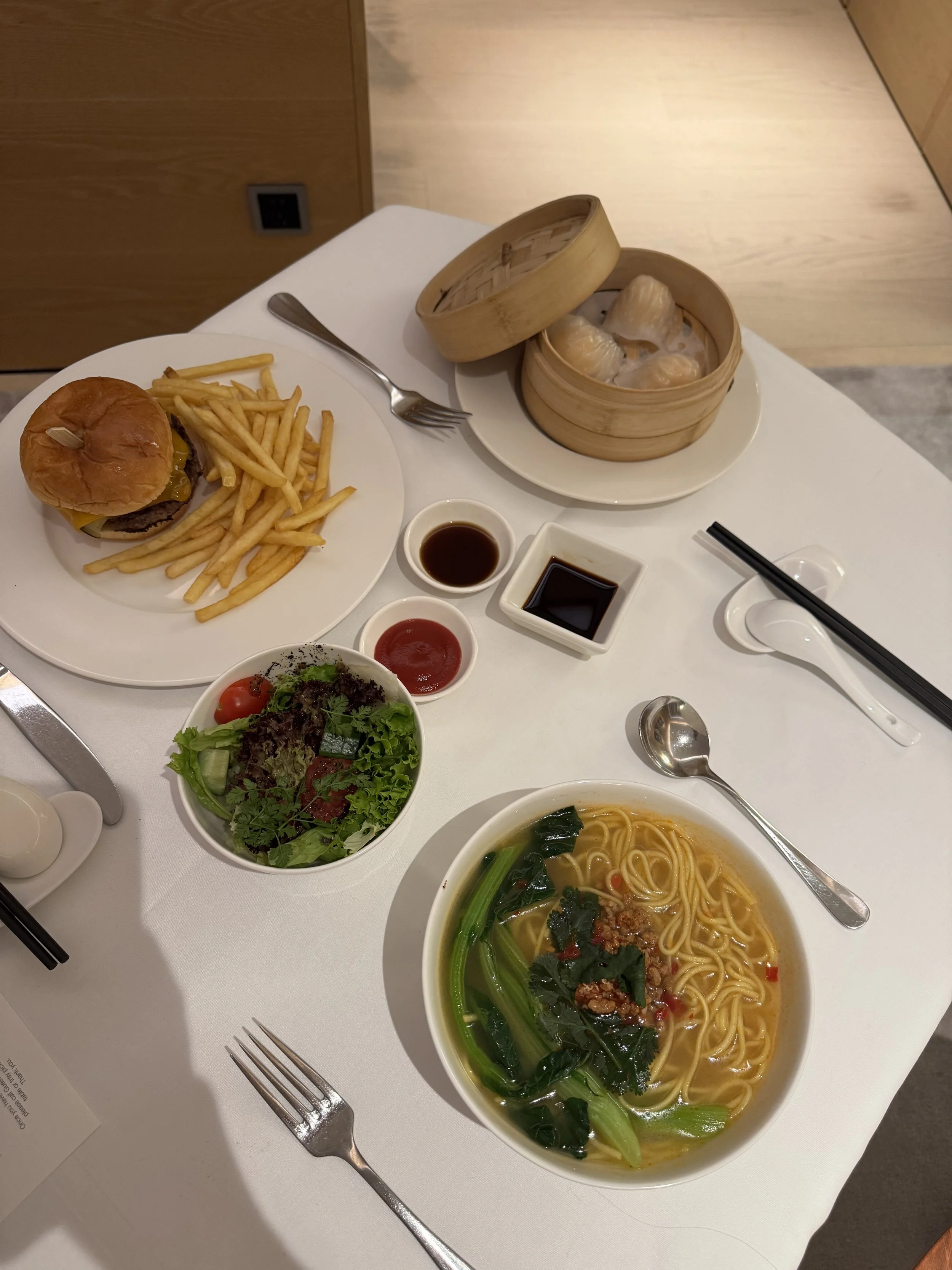 Room service table with burger and fries, noodle dish, salad, and dim sum