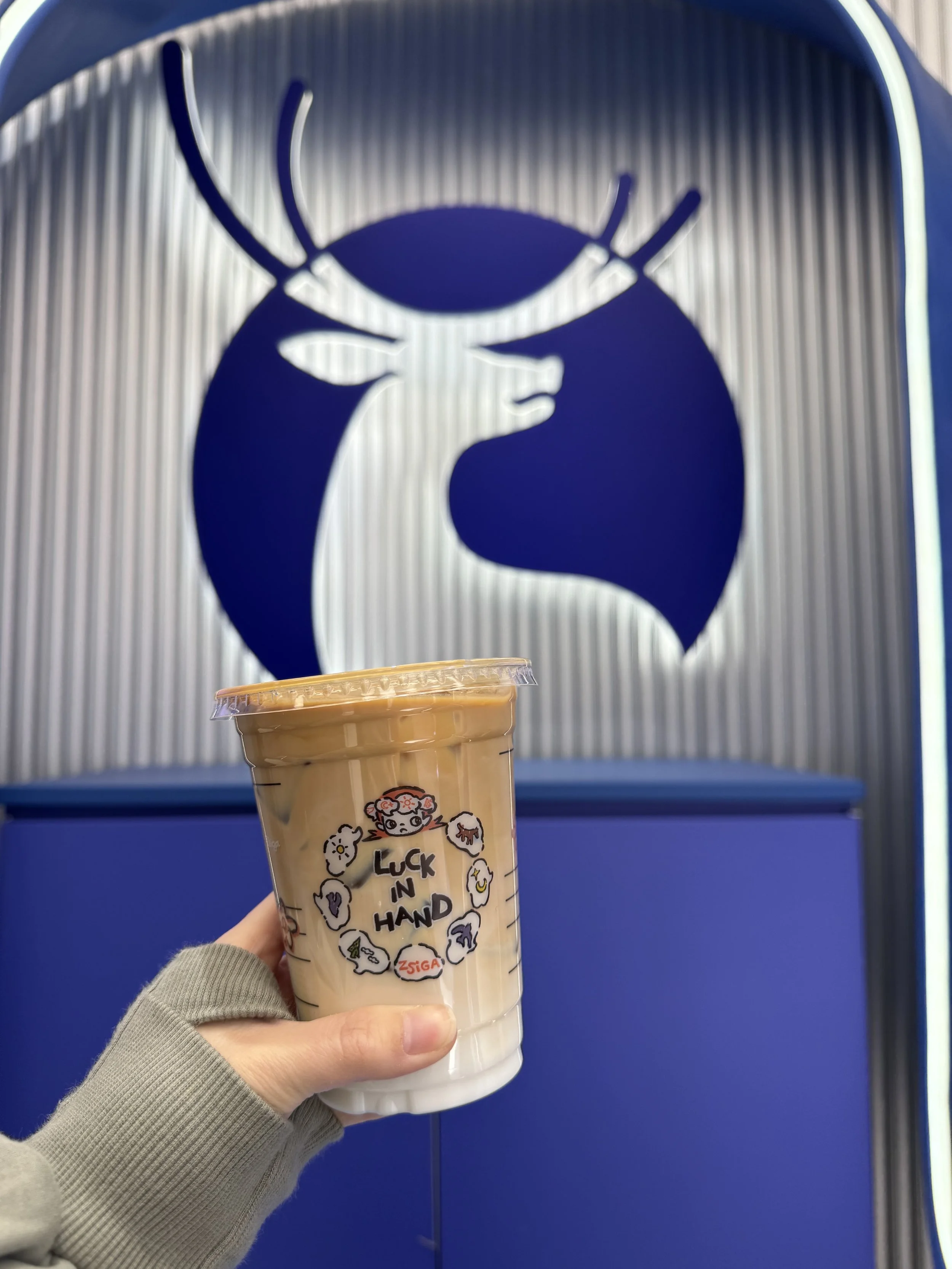 Iced coffee in a clear plastic cup in front of a blue logo with a deer