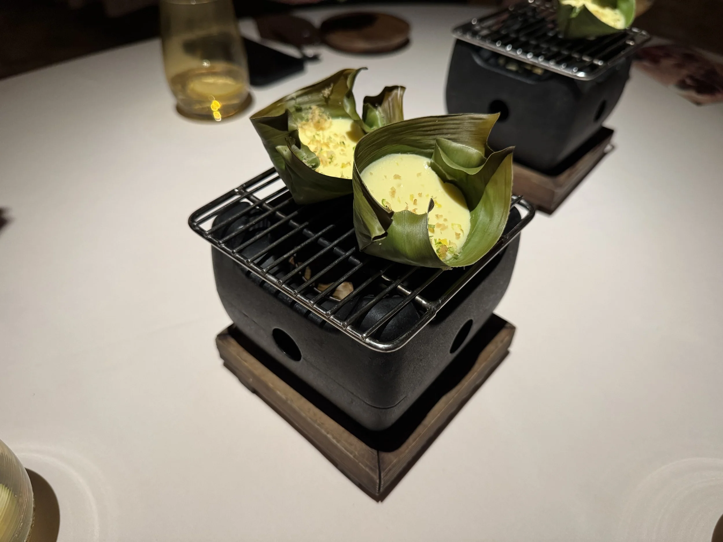rice cake topped with egg yolk in a banana leaf boat on a black stone grill