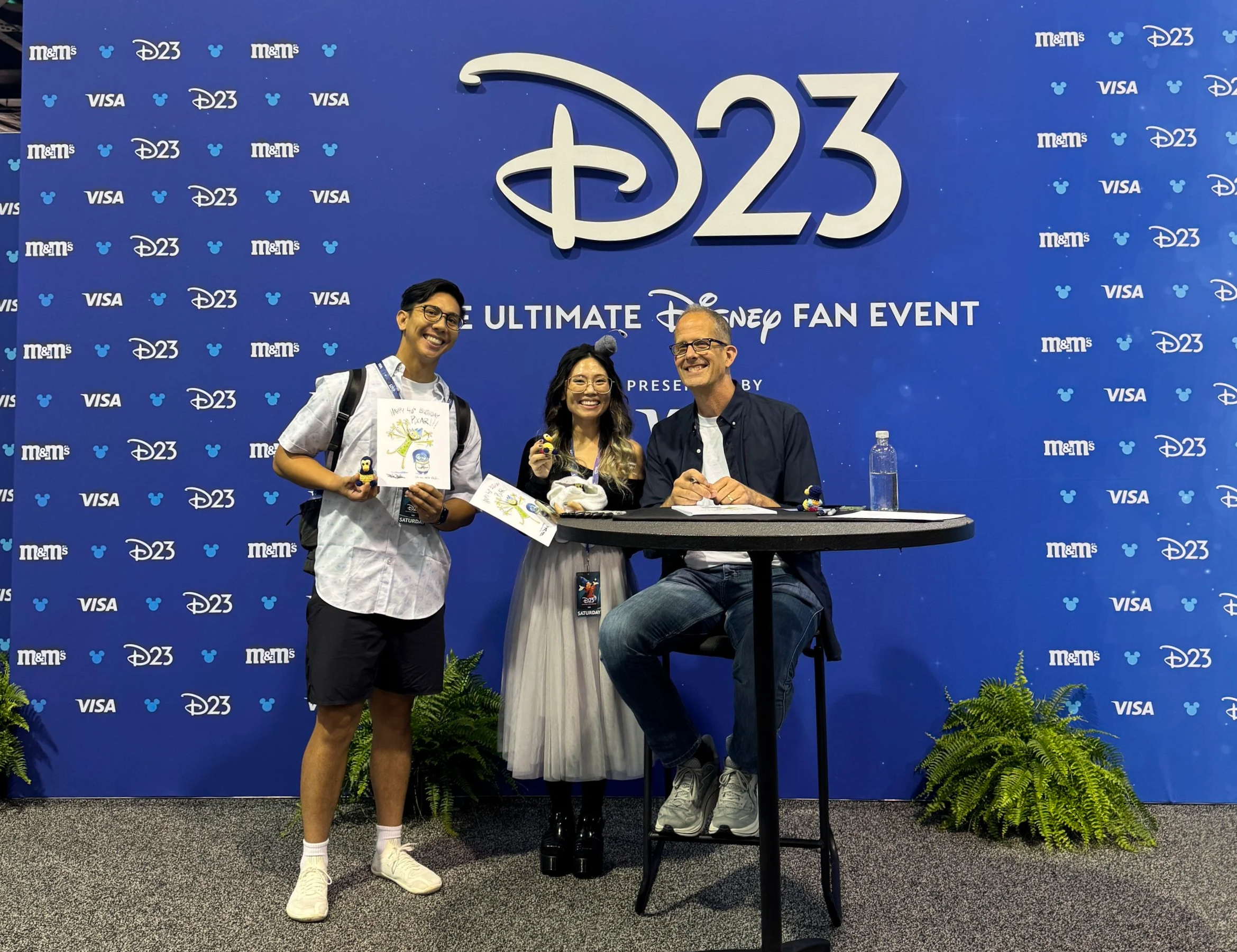 Standing next to Pete Docter in front of a D23 sign holding signed prints