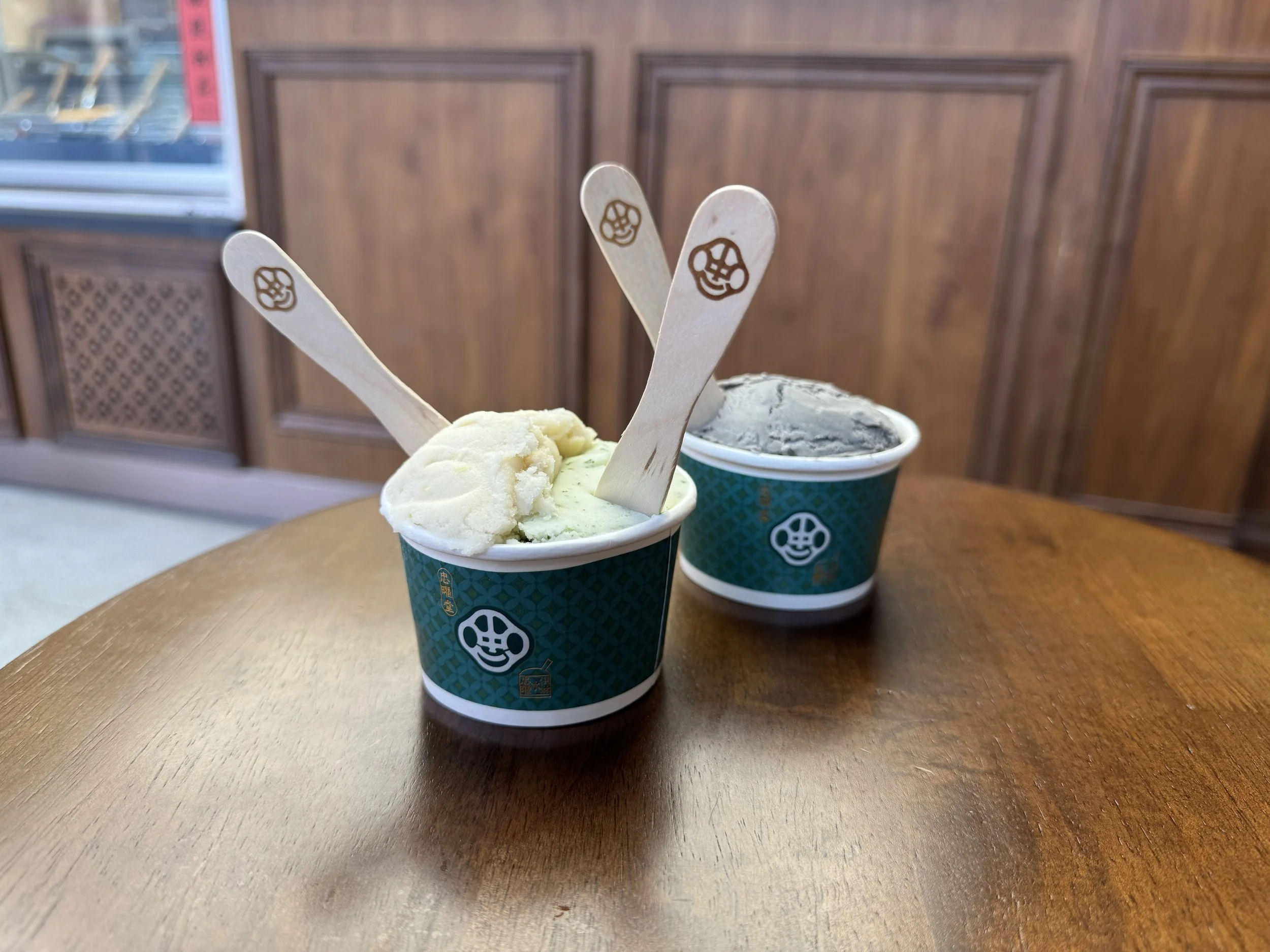 Two small cups of gelatin with wooden spoons sticking out on a wooden table