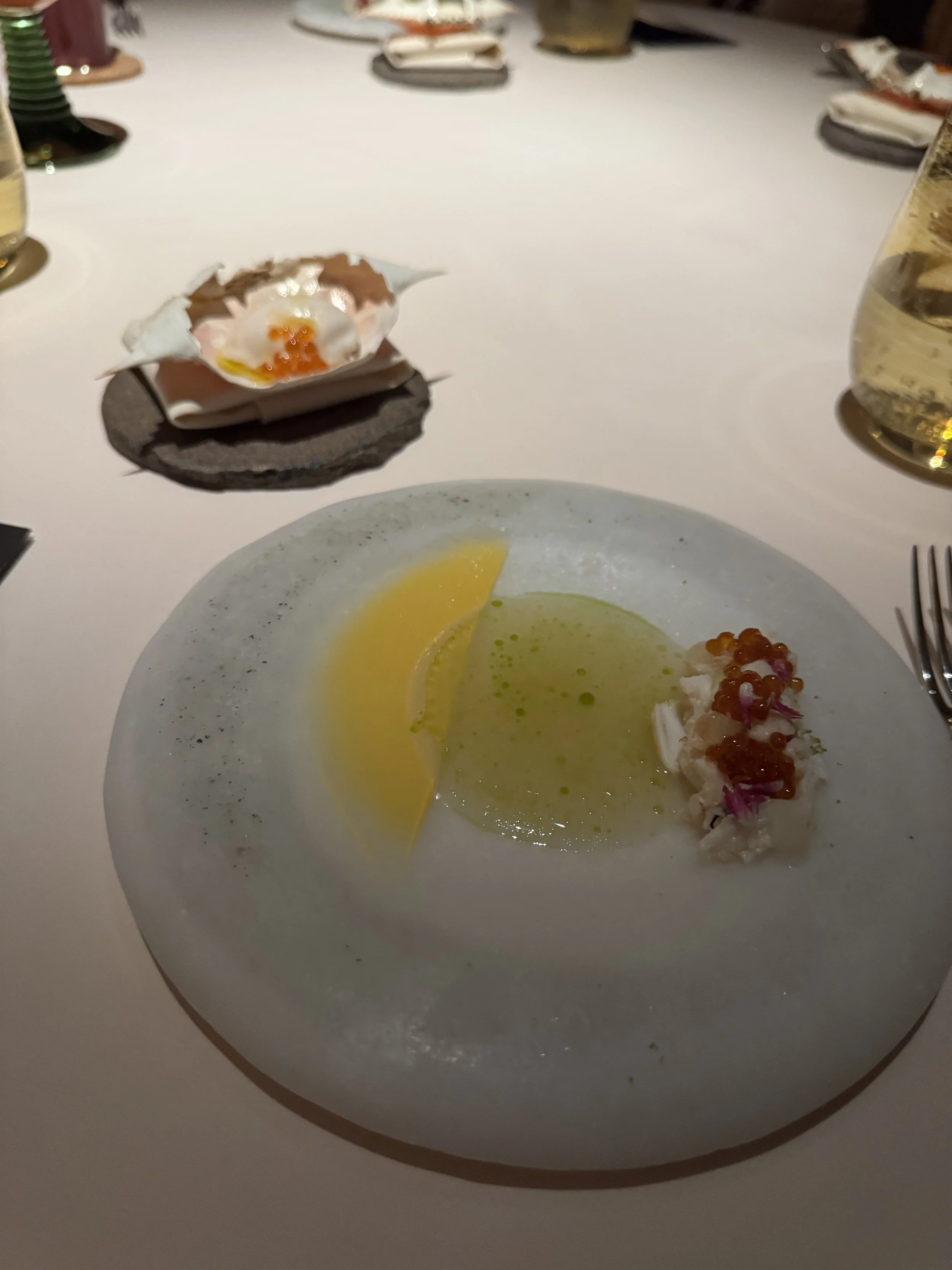 crab meat topped with Ikura on a white stone plate with green lime gel and emulsified crab fat with a small crab shell in the background with a crab ice cream inside