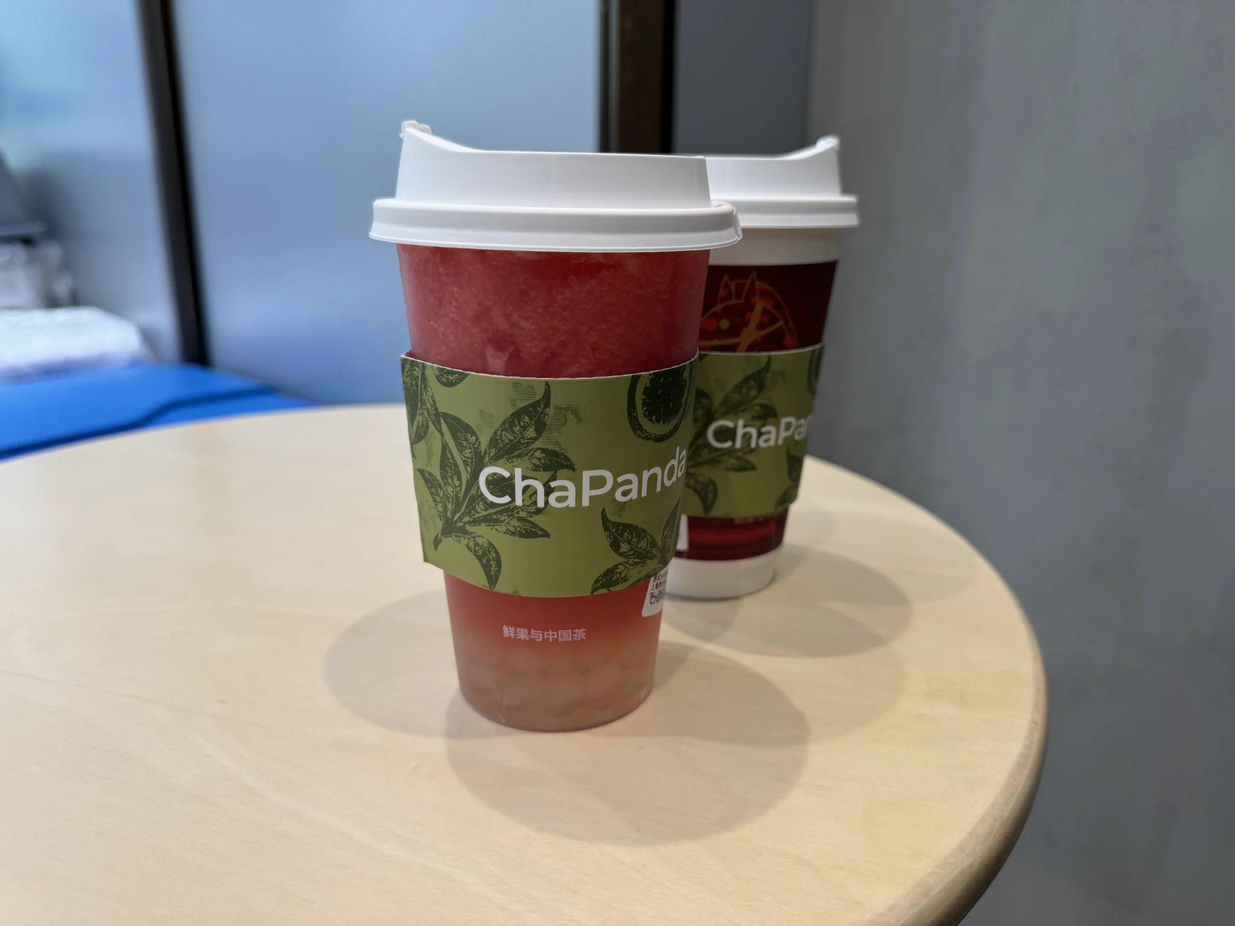 Cup with blended watermelon with white agar pearls in front of another cup with a chapanda cup sleeve on a table