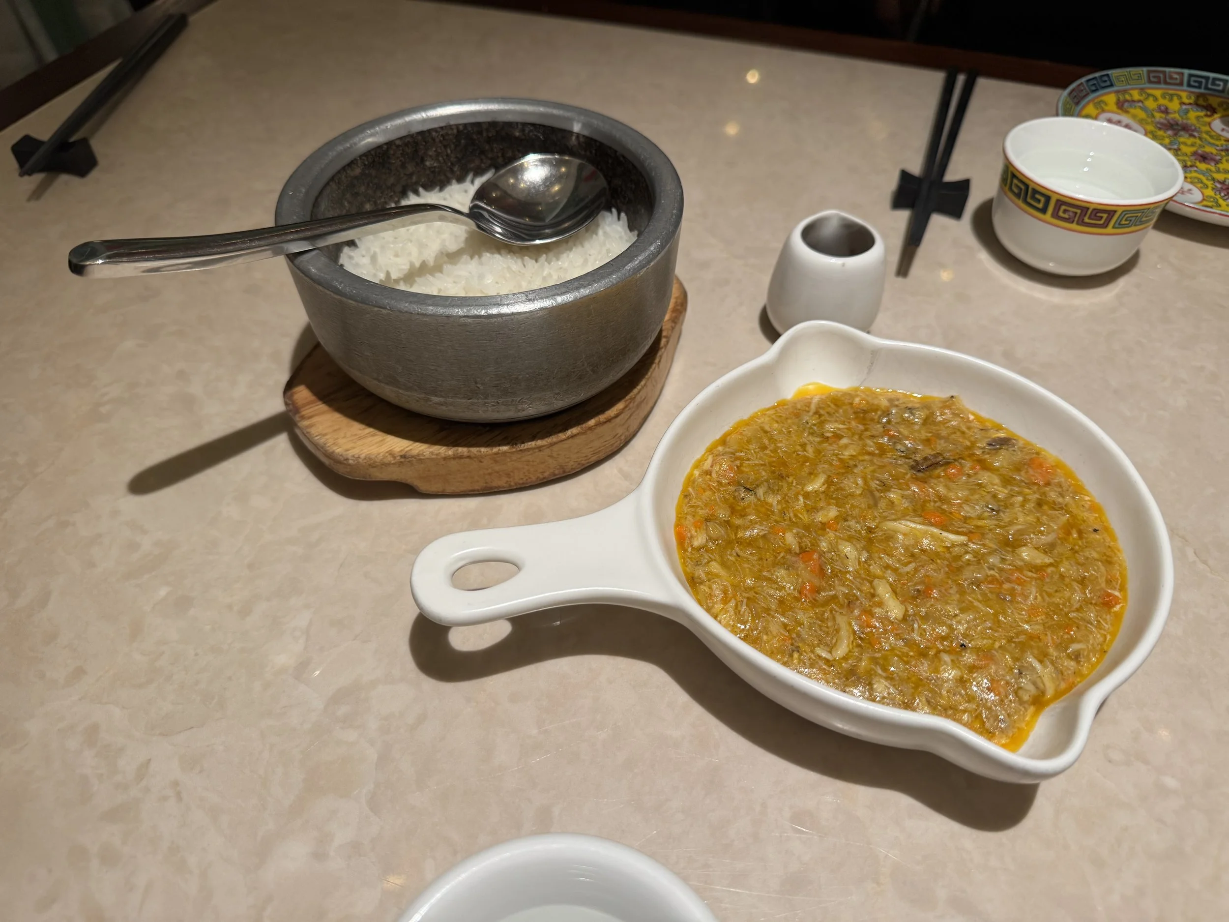 Crab roe sauce in a white bowl next to a bowl of rice in a claypot