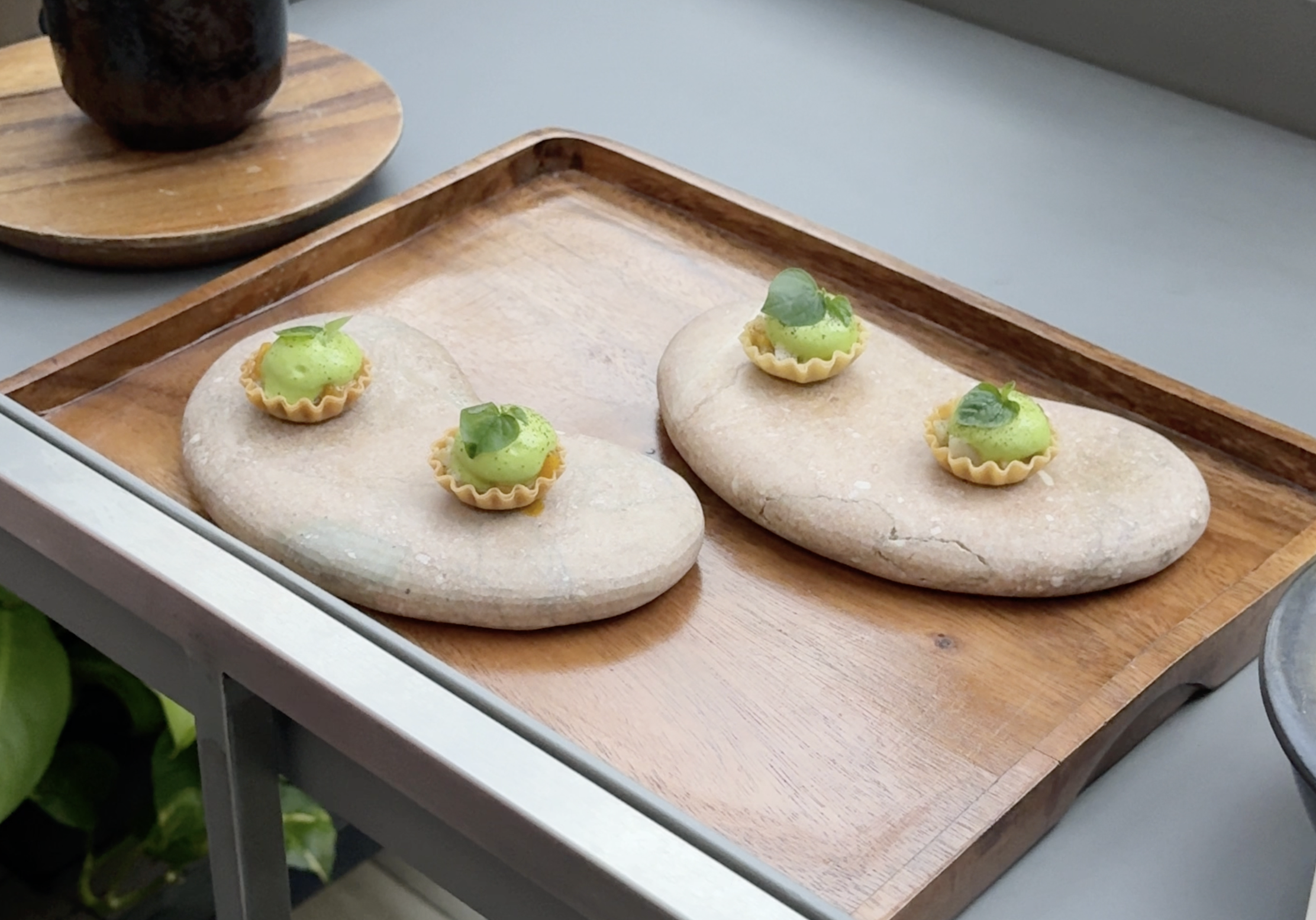 Four mini tartlets with green filling on oblong stone plates