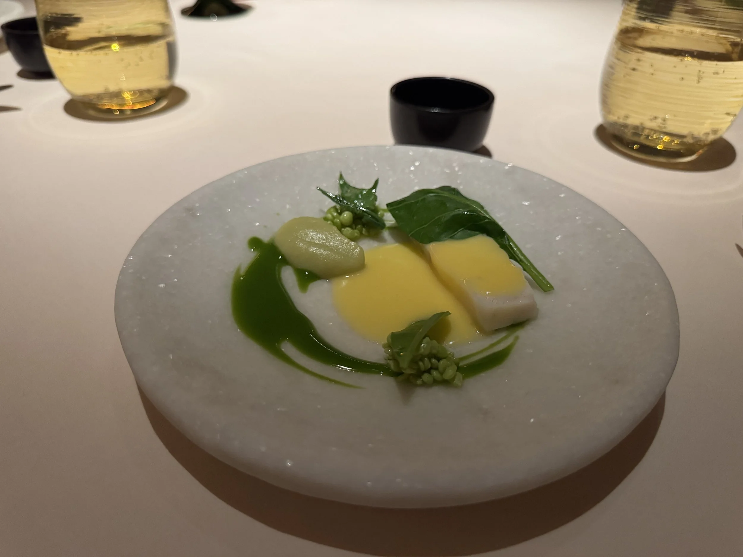 Sliced piece of grouper on a white stone plate with green garnish from vegetables and puree