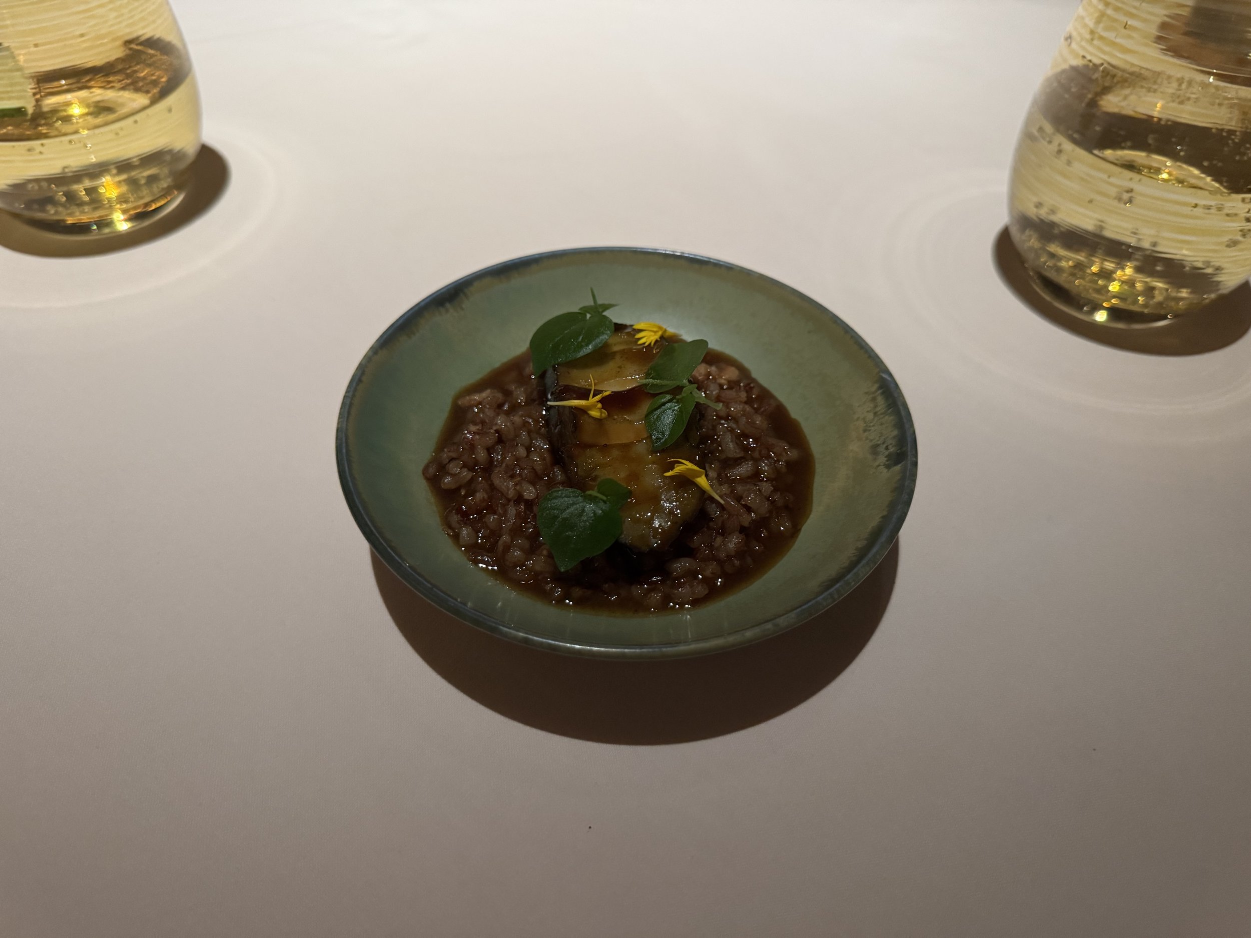 Small green plate with sliced abalone in a bed of rice porridge topped with green garnish