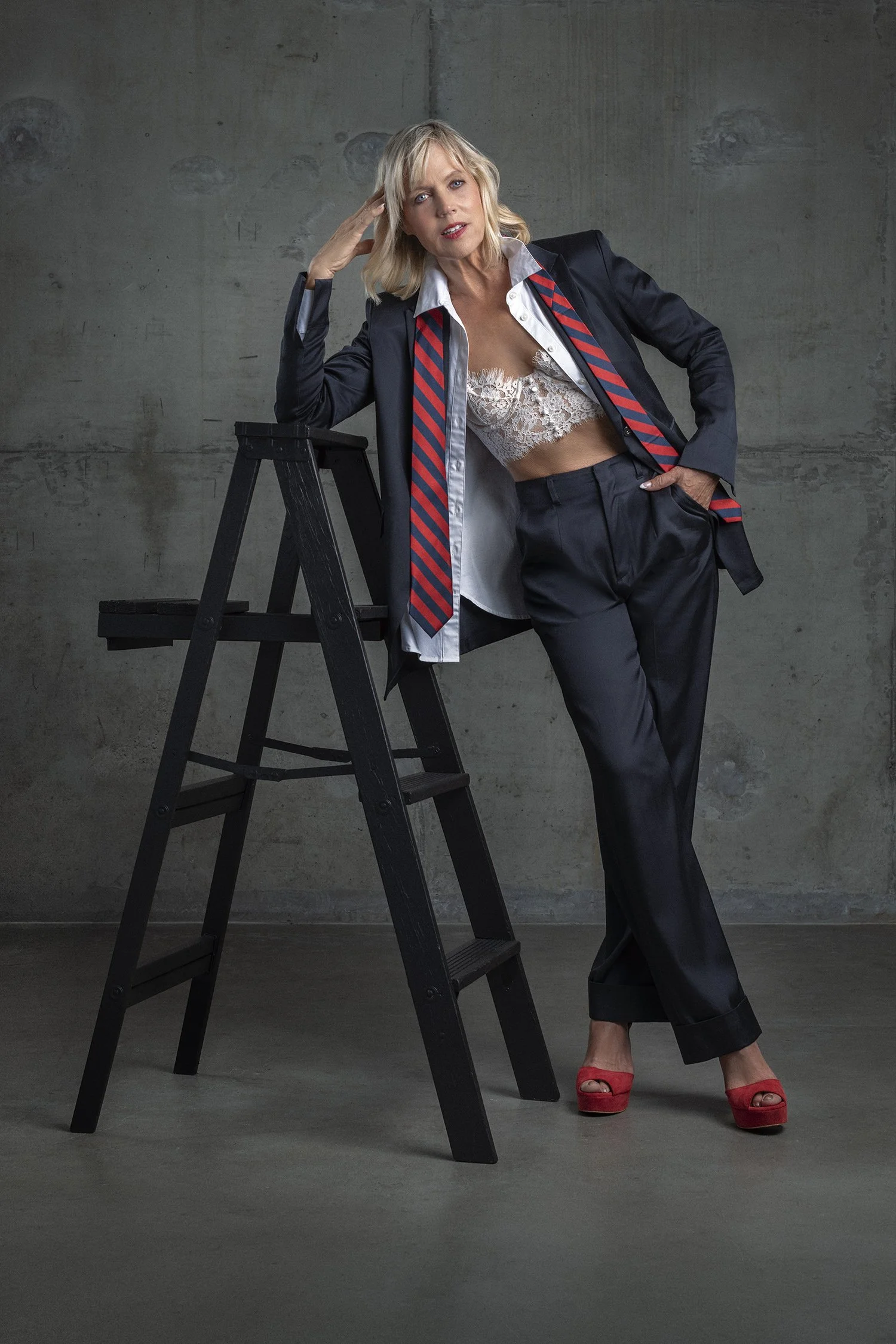 Catherine Grace O'Connell with blonde hair photographed in an editorial fashion style in studio wearing Elaine Kim Collection navy blue suit and blazer and red and blue striped men's tie photographed in Seattle, Los Angeles and New York. Ageless in S