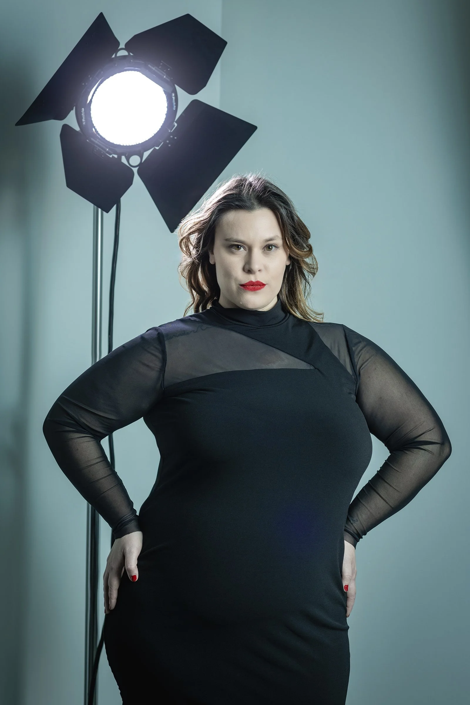 Plus size woman in black dress with movie light backdrop on set photographed in Seattle, cyan toned background.  Profoto lighting equipment with grid and barn doors.