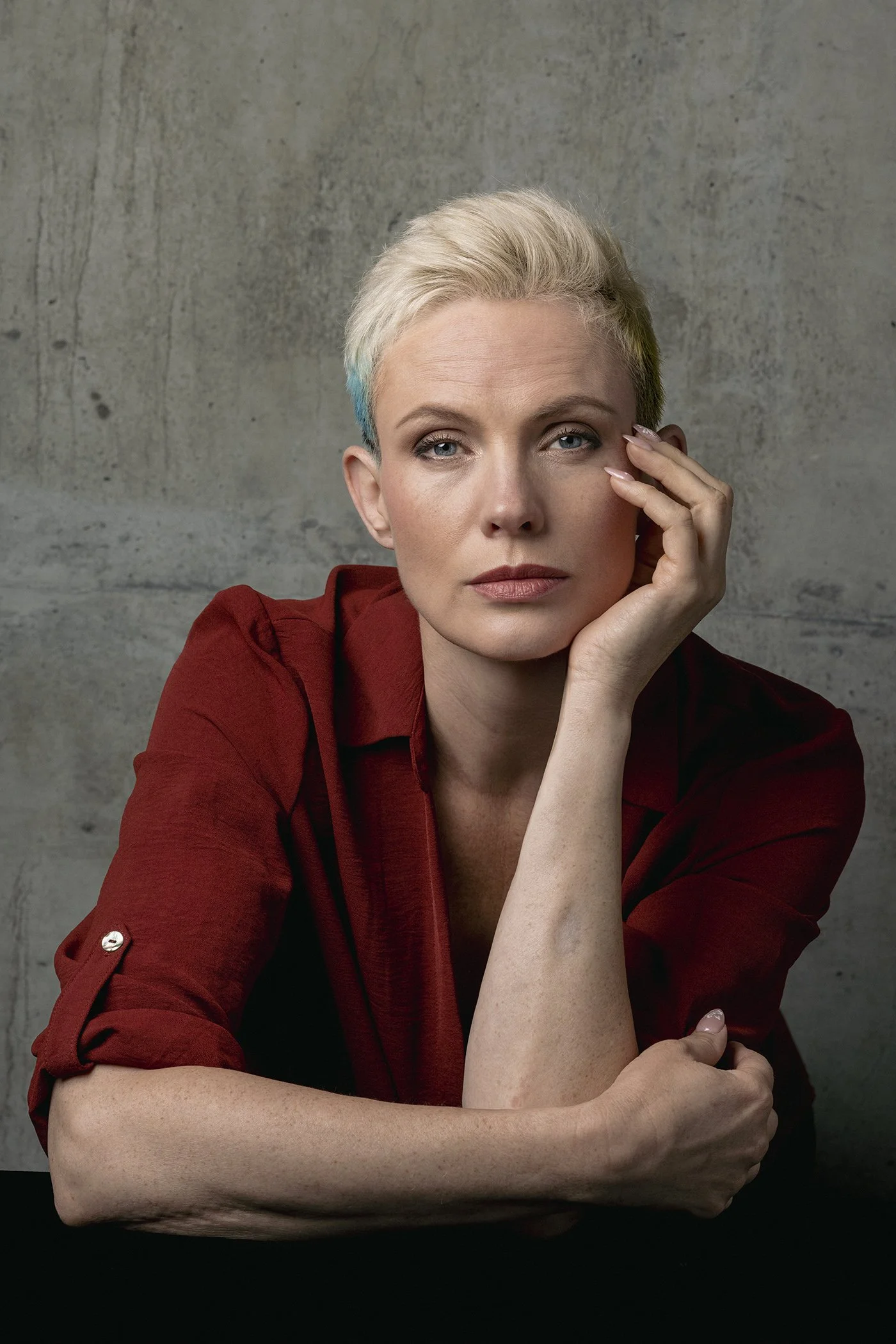 Profoto studio portrait of woman with bleached blonde hair wearing rust toned blouse photographed in studio against concrete wall in Seattle Los Angeles and New York