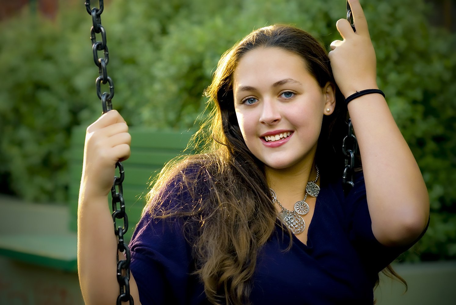 High school senior portrait of woman on swing in Mission District San Francisco photographed in natural light with sun going down and back lit hair