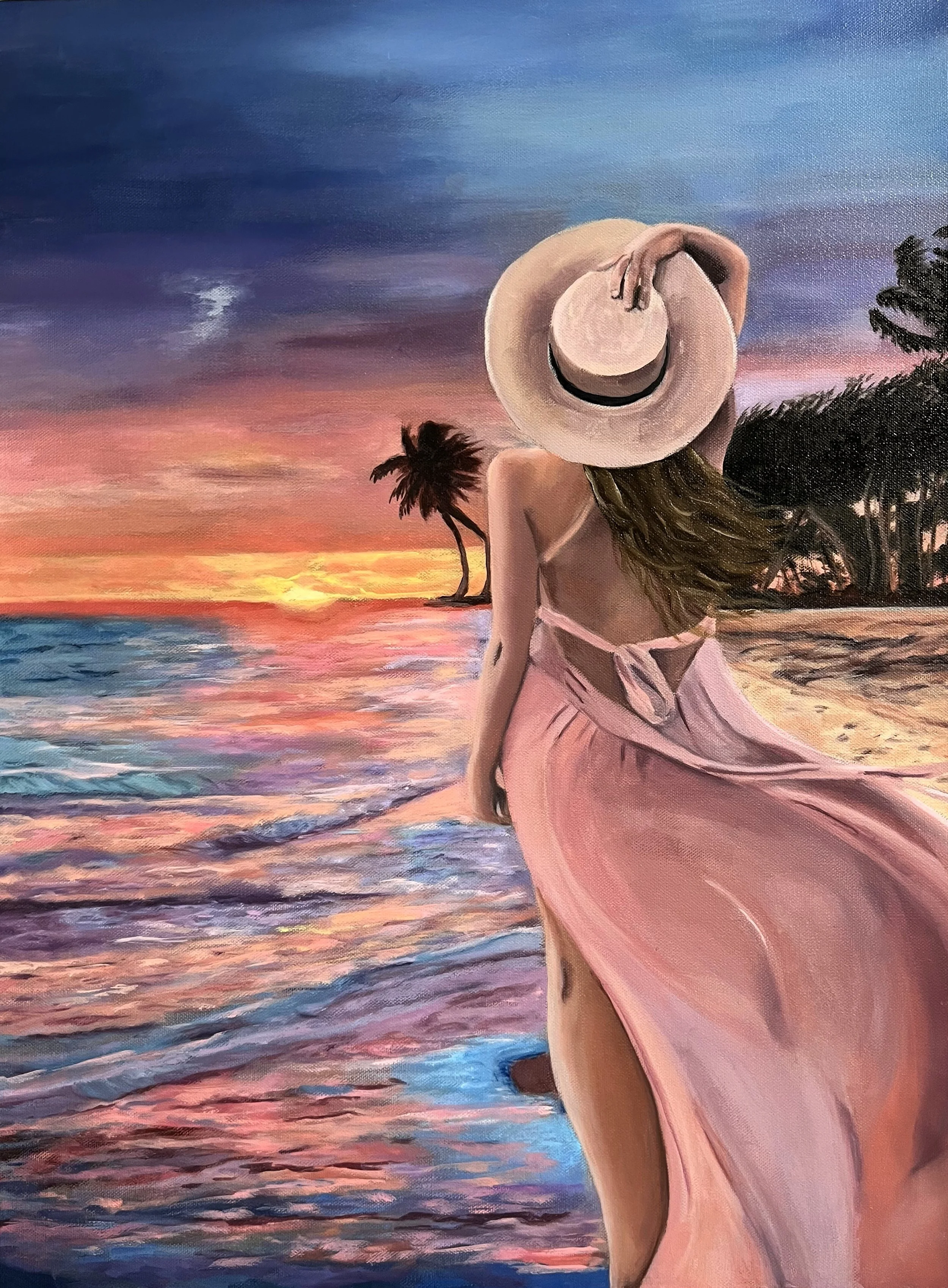 A woman in a pink dress and wide-brimmed hat stands on a beach at sunset, with tropical trees in the background and waves on the shore.
