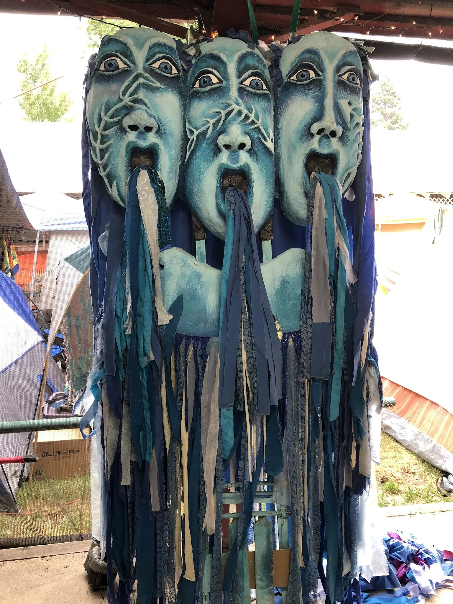 Three large blue masks with open mouths and streamers hanging down, displayed outdoors.