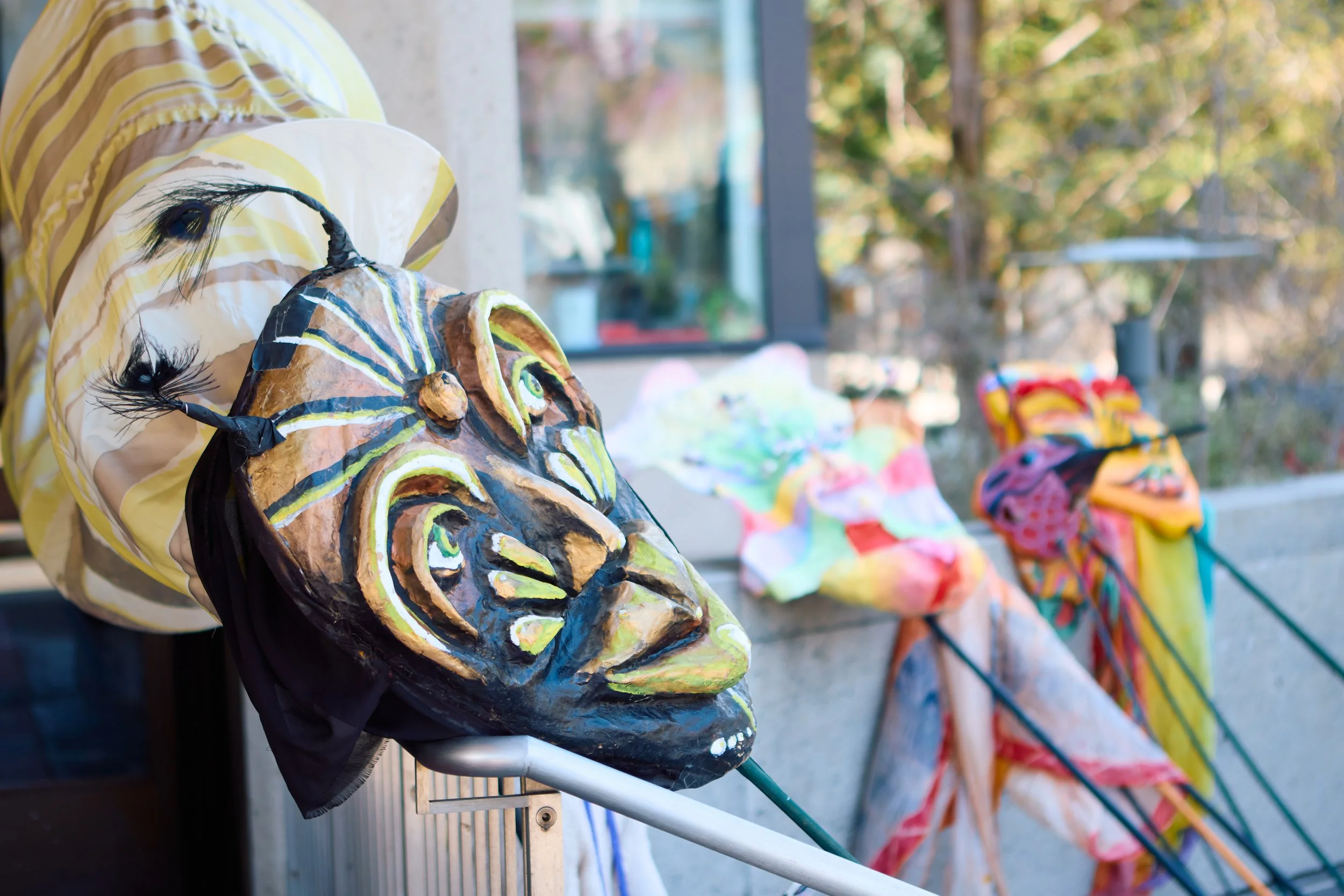 Colorful handmade masks and costumes displayed outdoors on a sunny day.