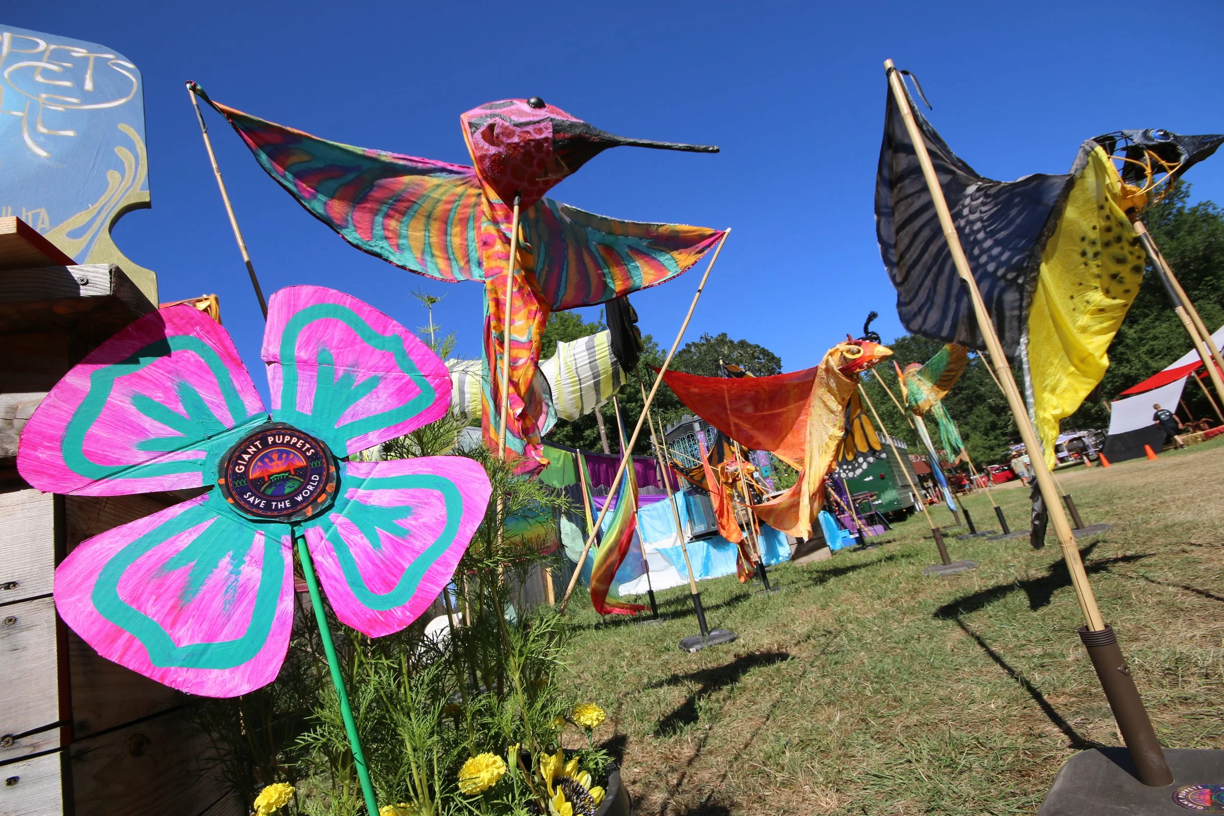 Colorful fabric dragon and butterfly-shaped pinwheels displayed outdoors at a fair with tents and trees in the background.